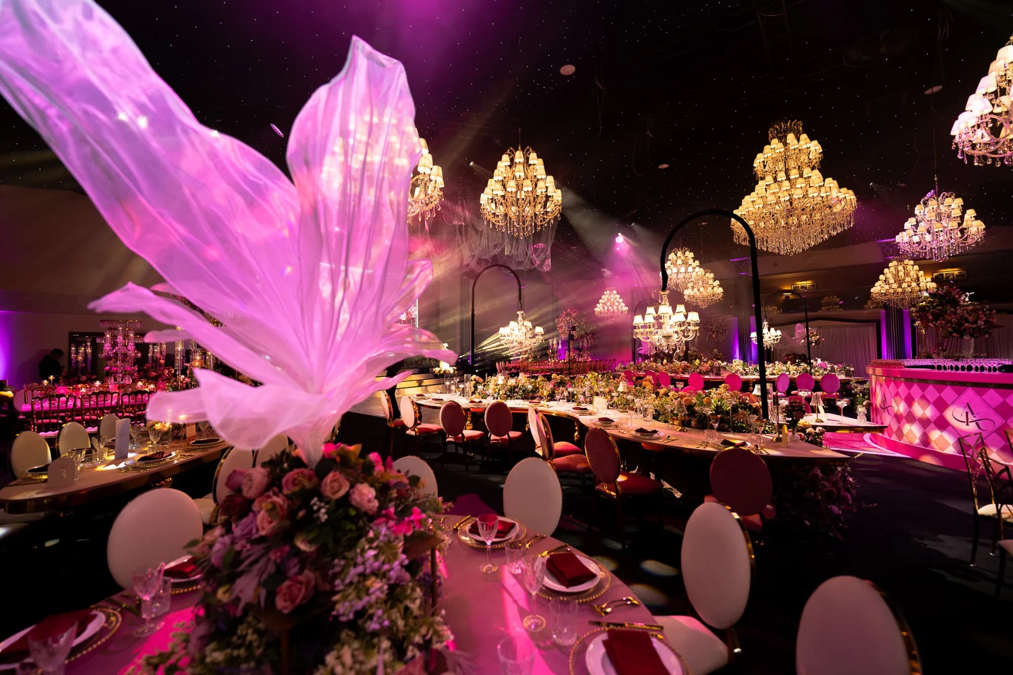 Pink-lit sculptural centrepiece and chandeliers over wedding tables at Dallas Burston Polo Club