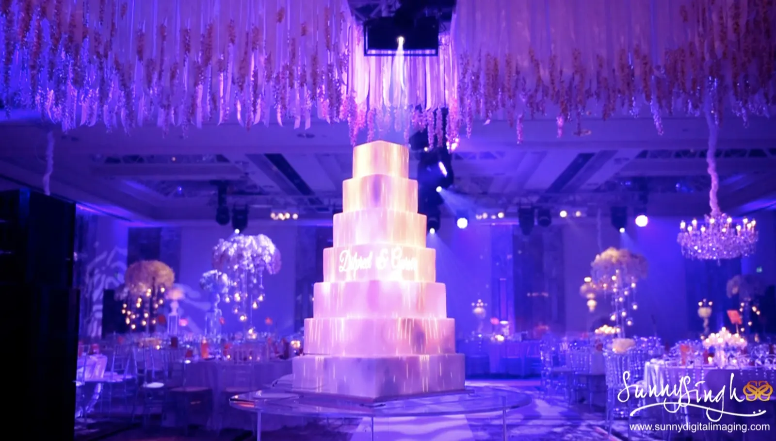 Tall tiered wedding cake beneath a floral canopy in purple lighting | Claridge's Tall tiered wedding cake beneath a floral canopy in purple lighting at Claridge's