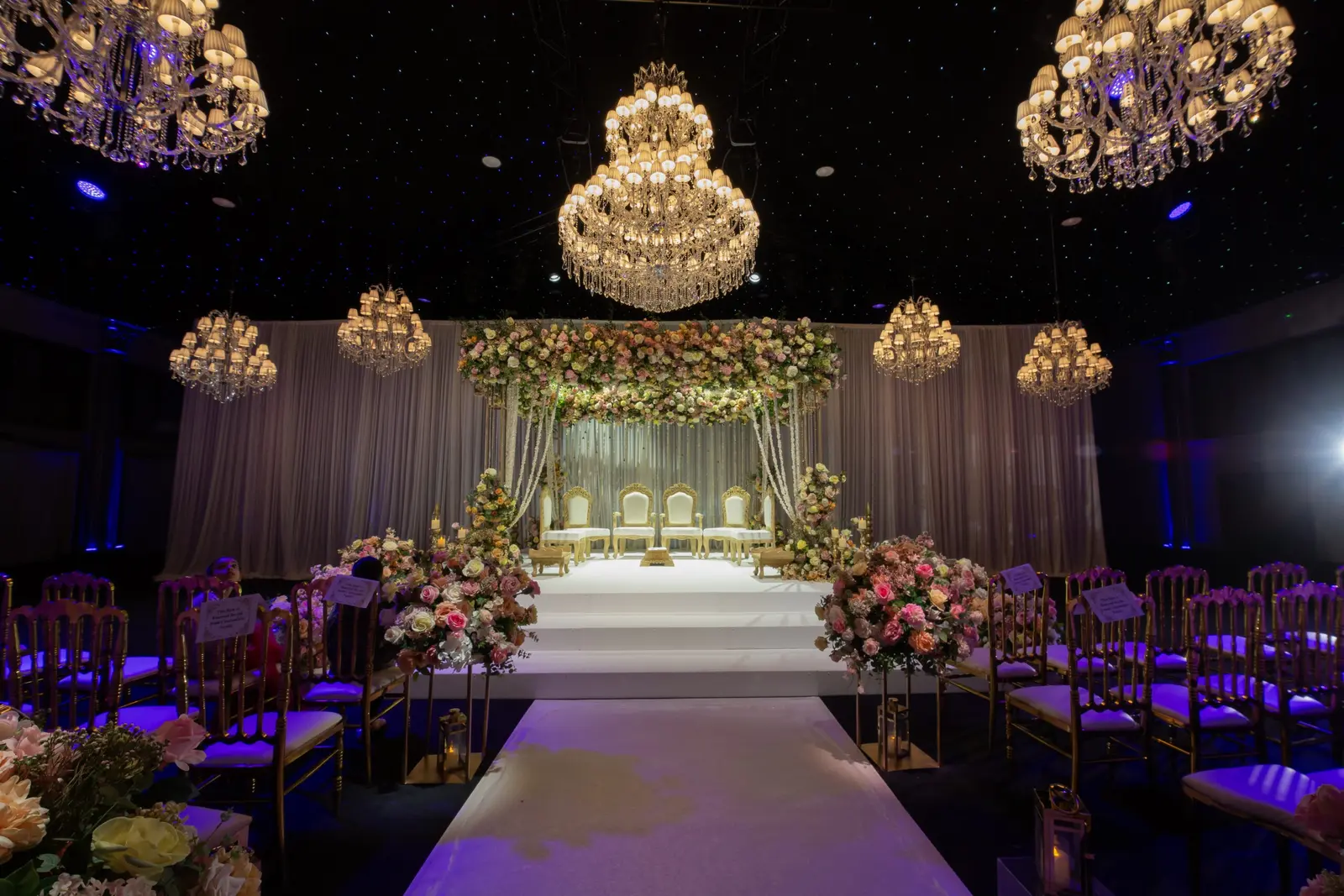 White ceremony aisle leading to a floral mandap beneath chandeliers at Dallas Burston Polo Club