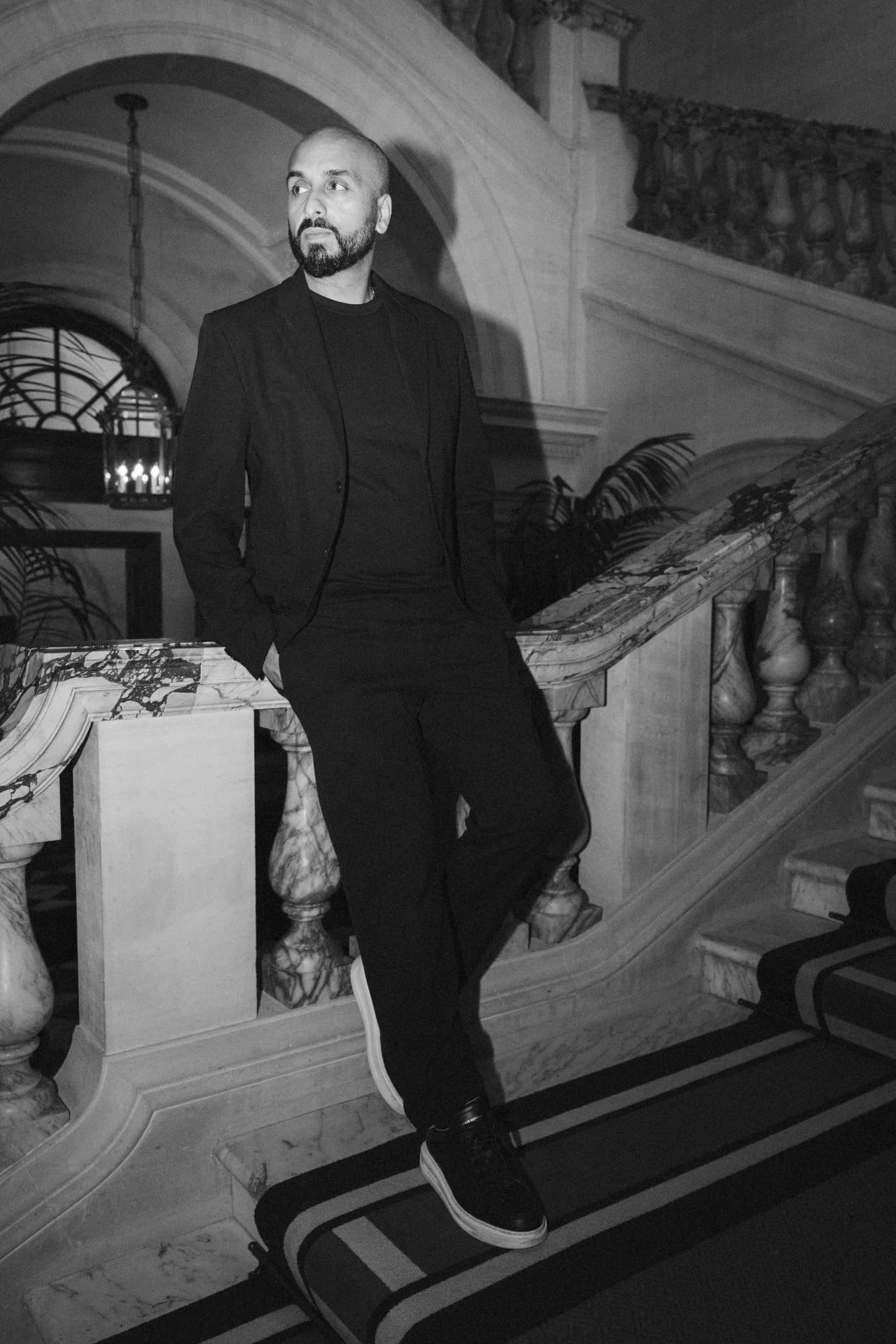Black and white portrait of DJ H of Kudos Music leaning on a grand marble staircase