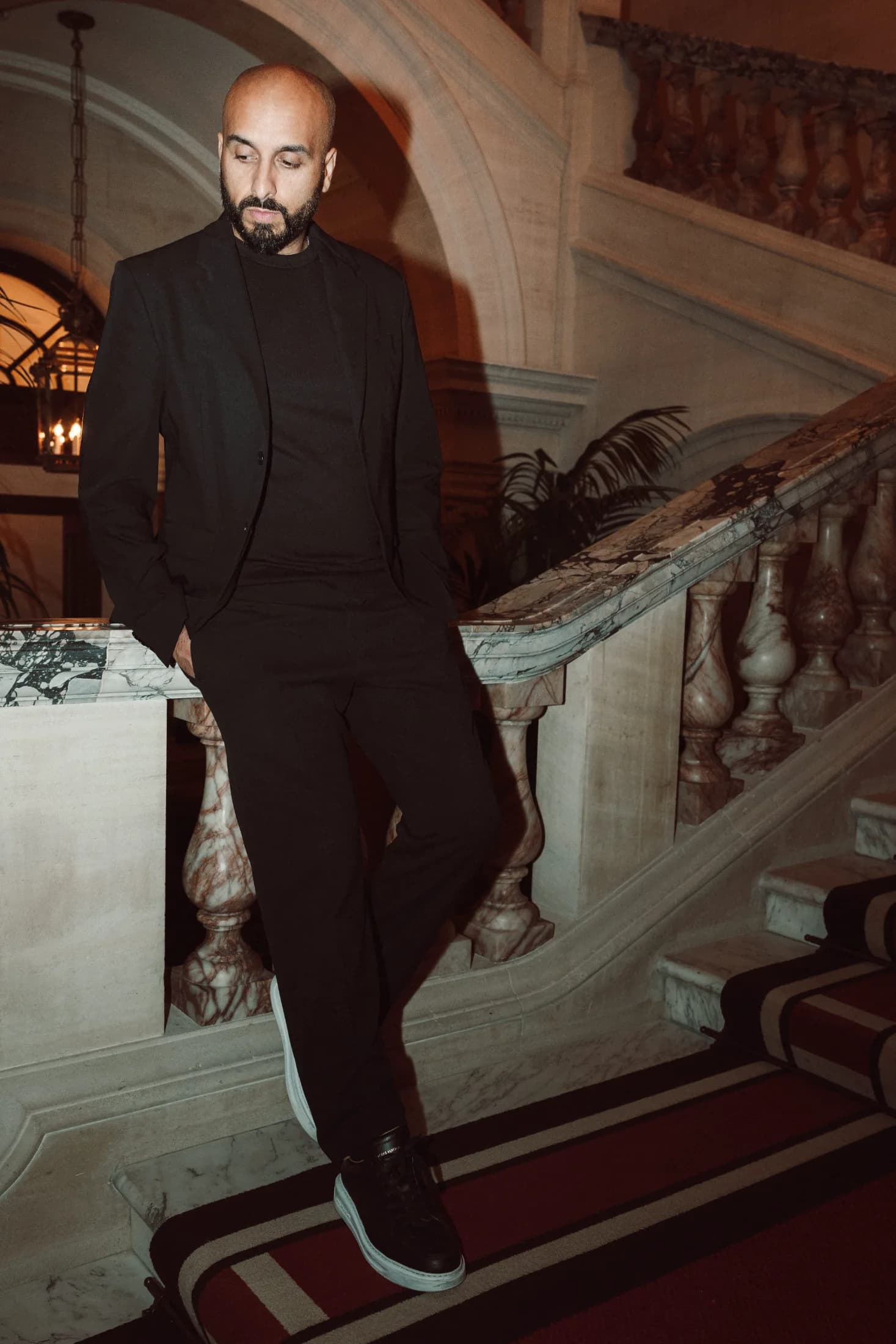 DJ H of Kudos Music in a black suit standing beside a grand marble staircase