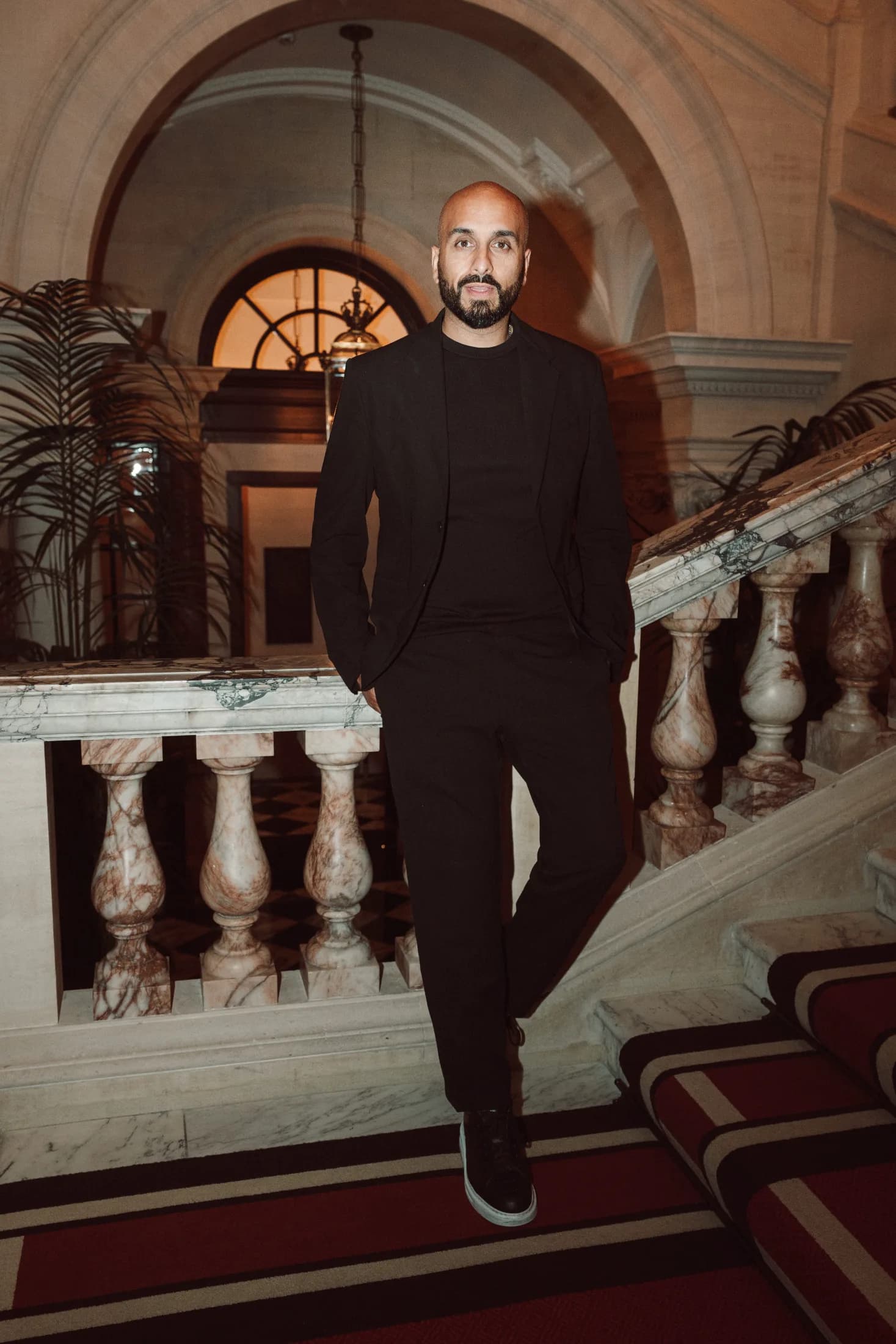 DJ H of Kudos Music in a black suit on the steps of a grand marble staircase
