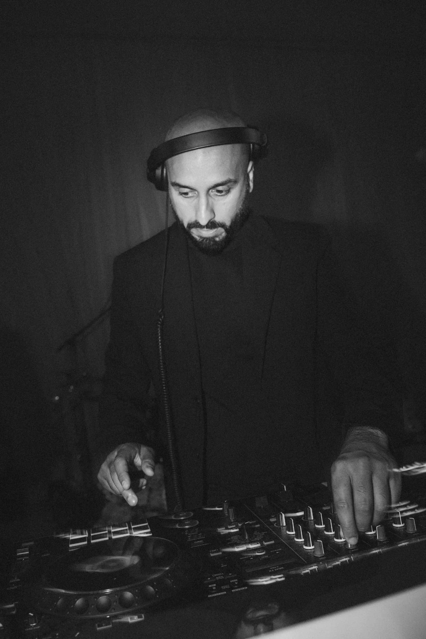 Black and white photo of DJ H of Kudos Music mixing on DJ decks wearing headphones