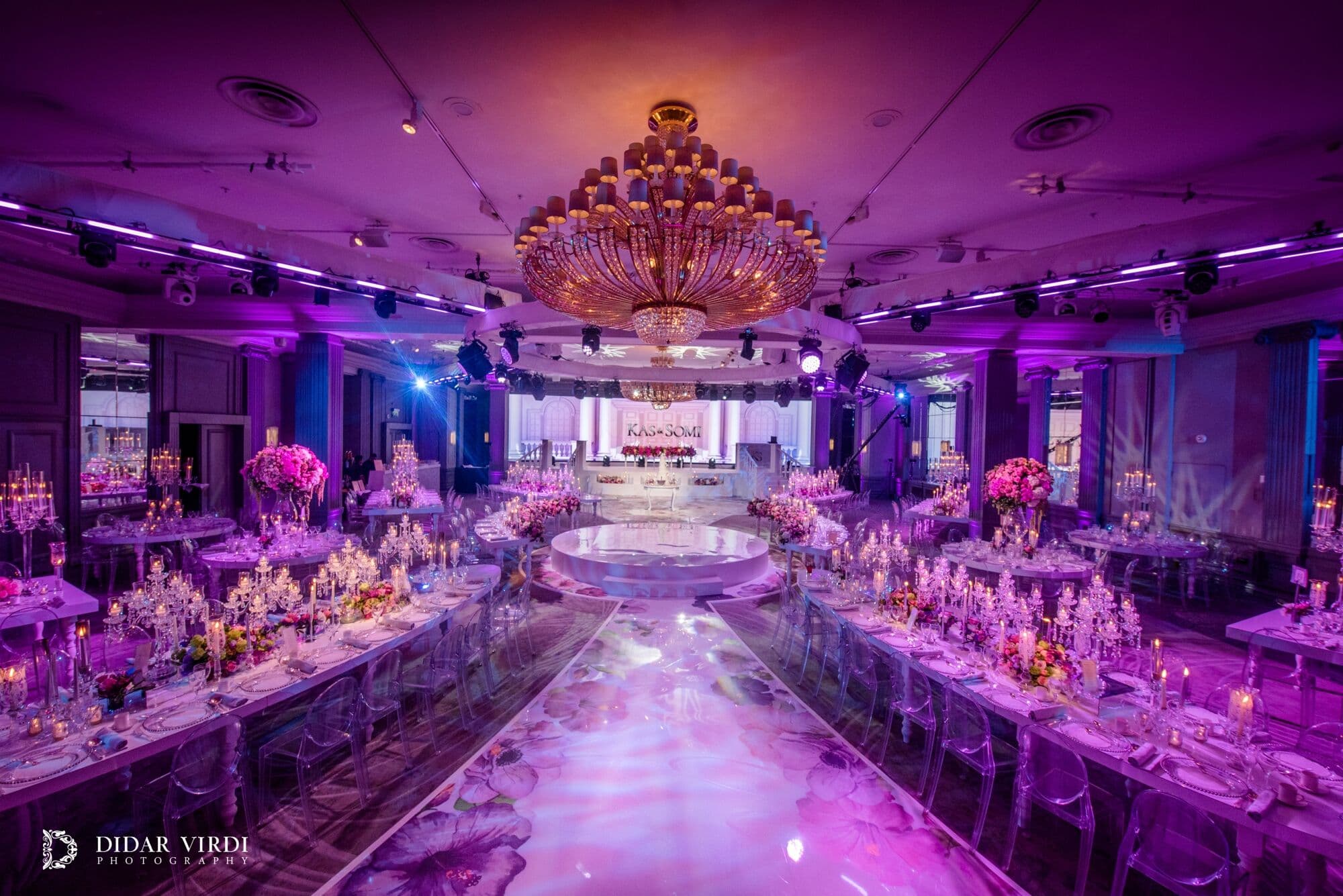 A ballroom ready for a wedding Wide view of Grosvenor House Ballroom with candlelit tables, chandeliers and purple wedding lighting.