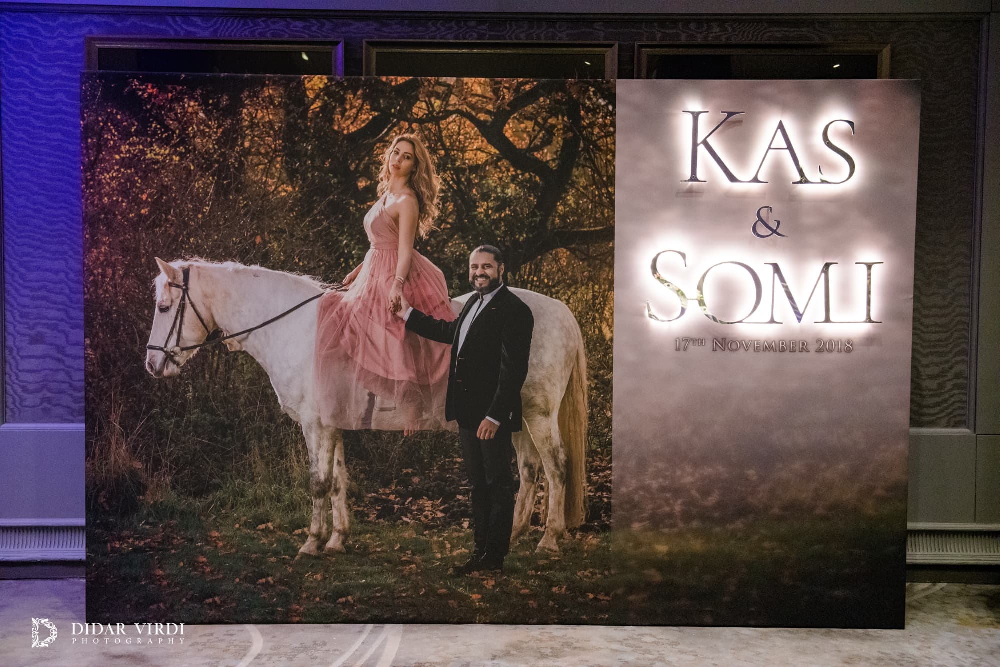 Wedding photo wall with a large portrait and softly illuminated lettering in the Grosvenor House foyer.