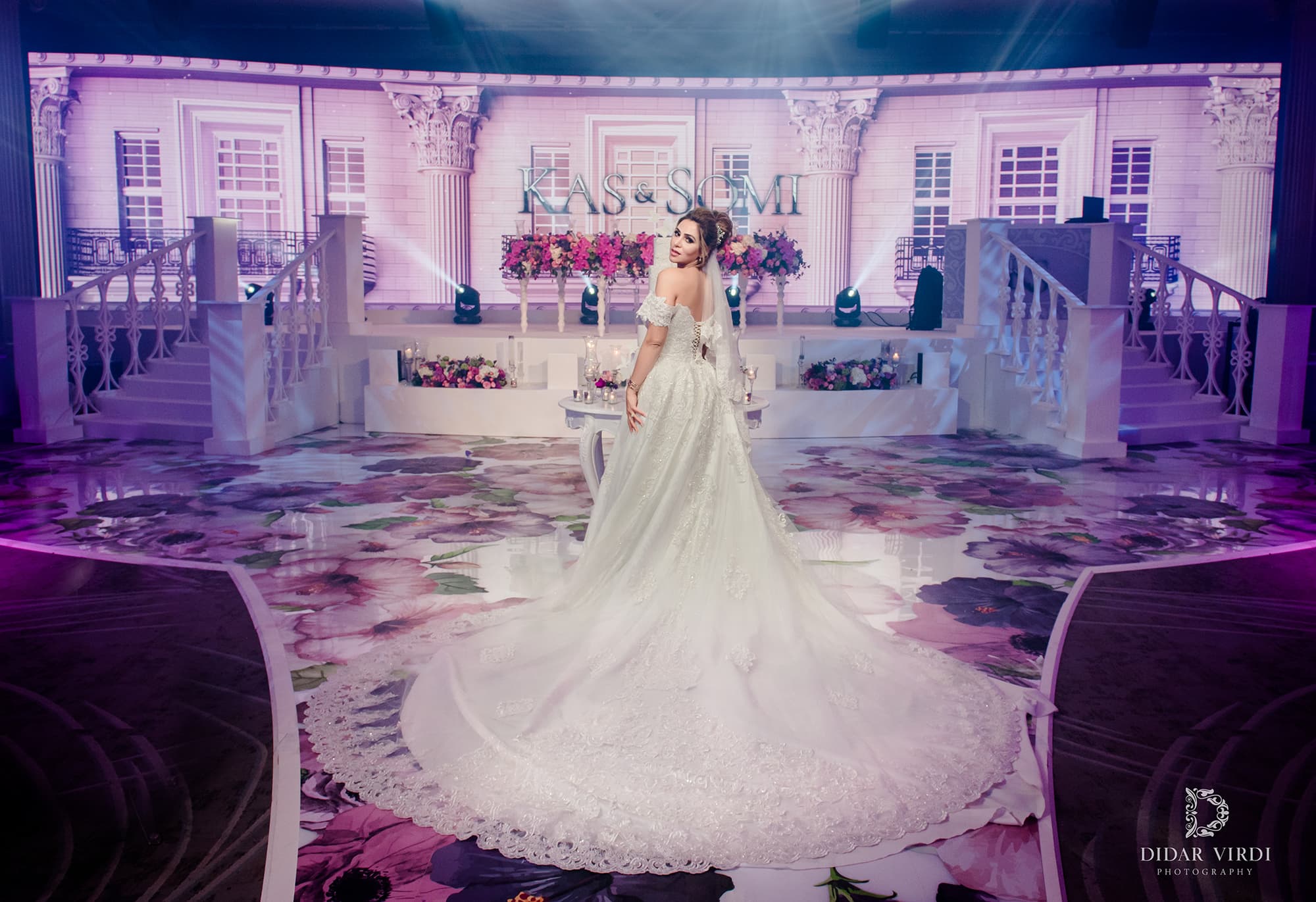 Bride in a white wedding gown on the floral walkway in front of the Italian-inspired staircase set at Grosvenor House Ballroom.