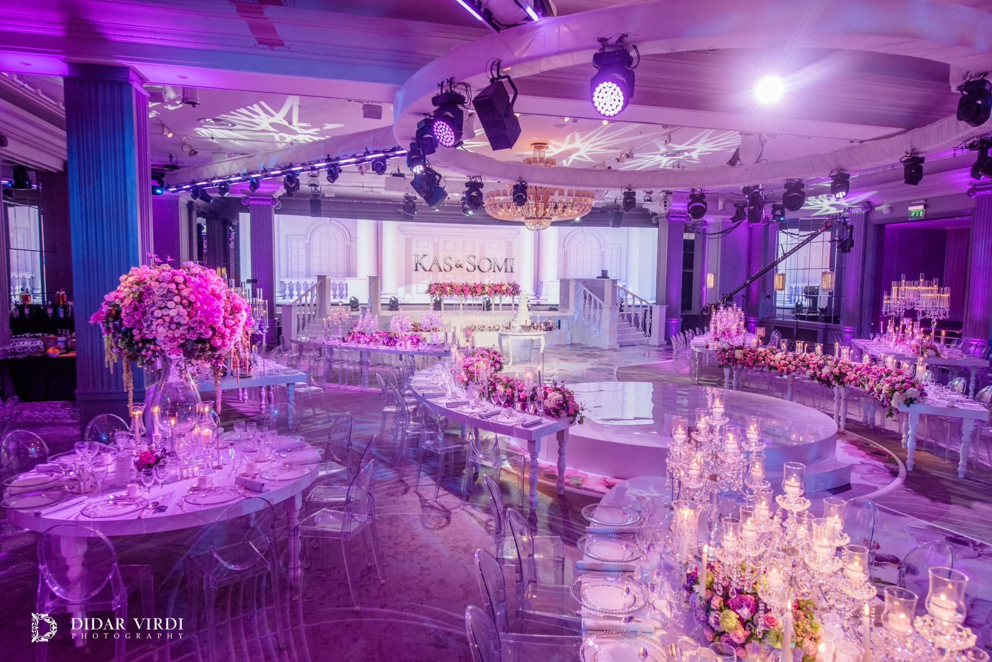 Dinner around the dancefloor Candlelit oval wedding tables with pink flowers and a white staircase backdrop at Grosvenor House London.