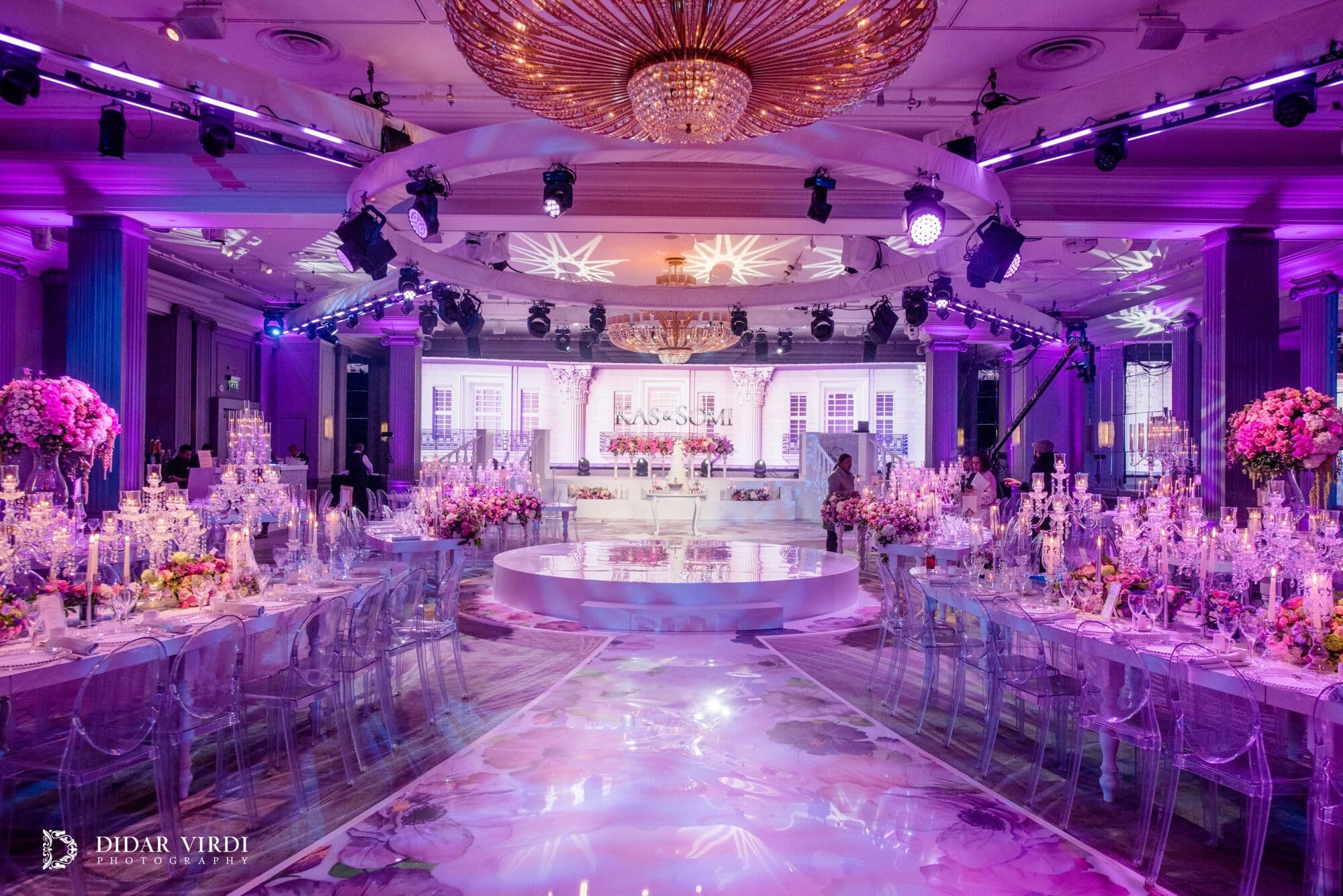 Pink and purple across the Ballroom Pink and purple wedding lighting over curved tables and a floral walkway at Grosvenor House Ballroom.