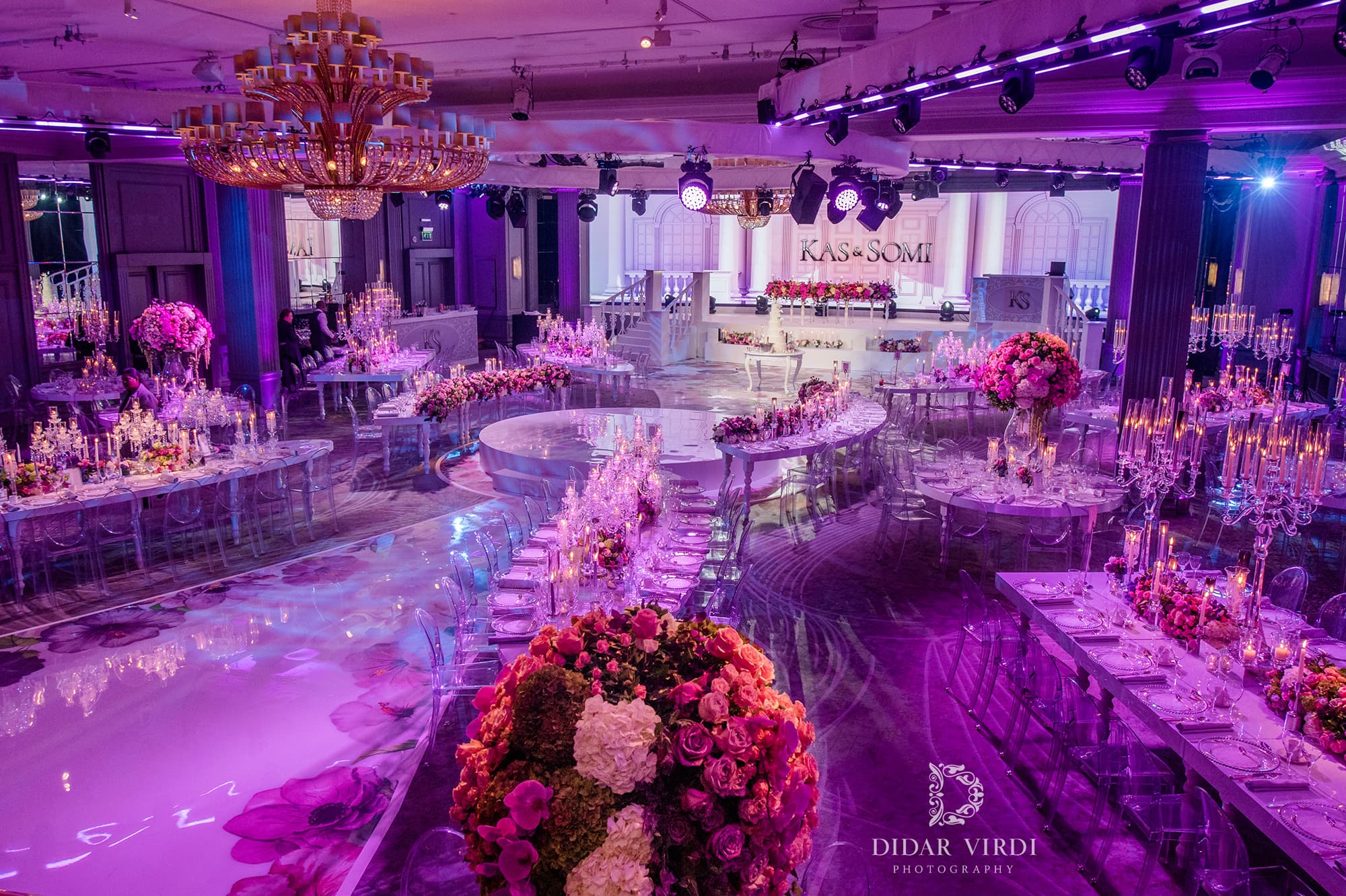 Tables that follow the room Long curved wedding tables with candles and pink flowers beside a floral walkway at Grosvenor House Ballroom.