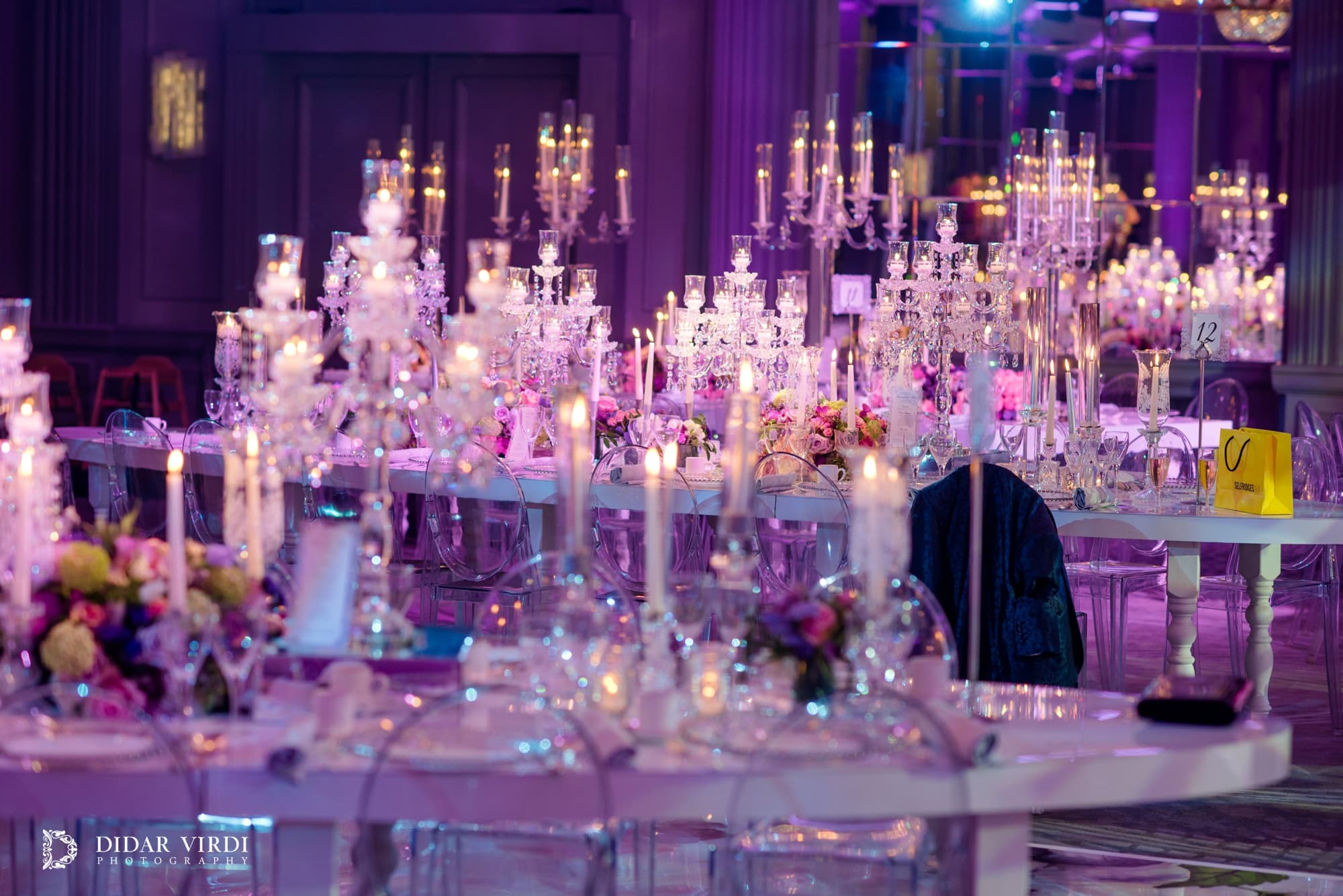 Glass candle holders, pink roses and place settings on a bespoke wedding table at Grosvenor House Ballroom.