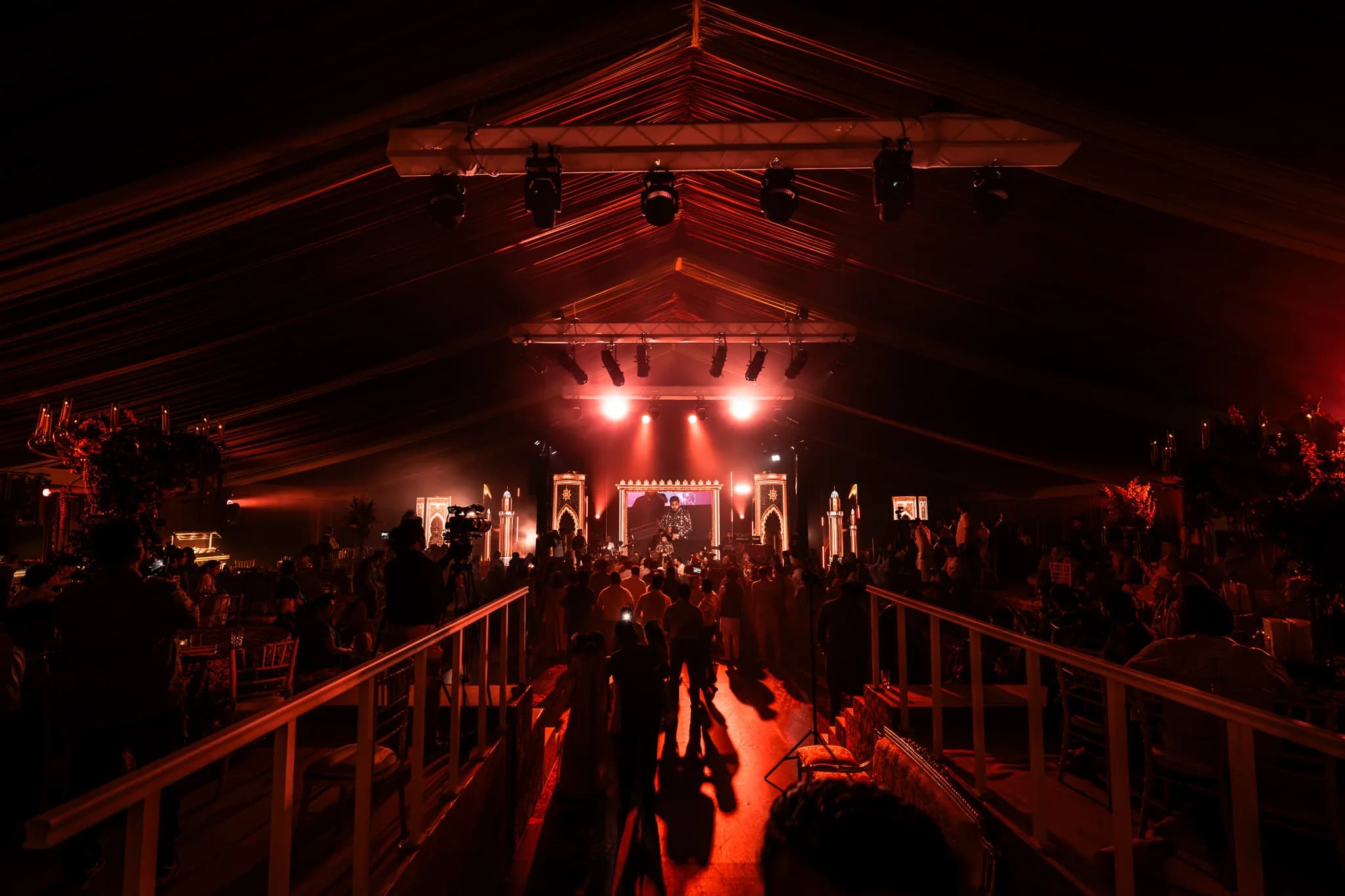 Looking down the railed walkway into the marquee at Eksimran and Dilraj's sangeet, the stage glowing red at the far end, Kudos Music
