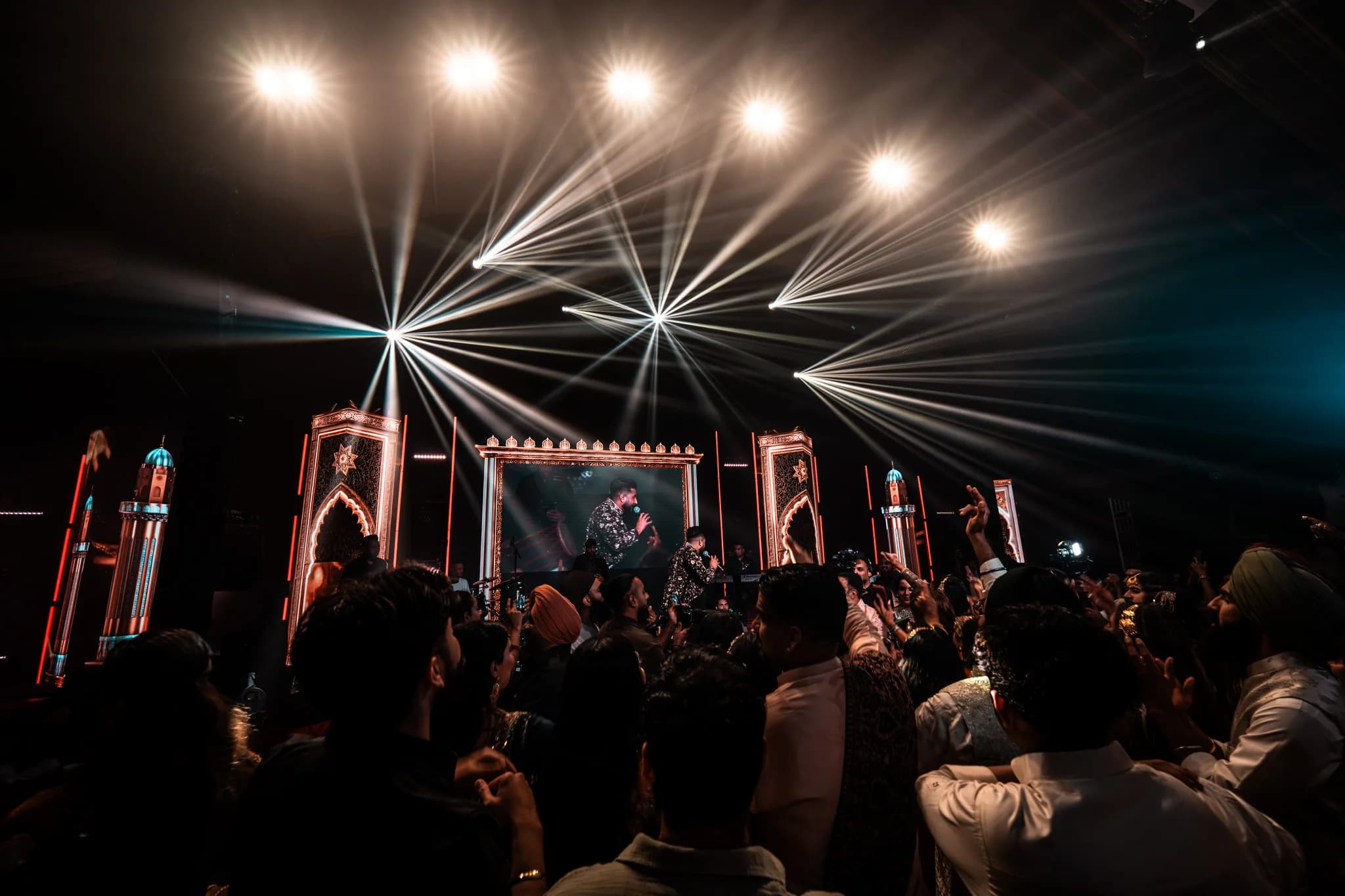 Guests pressed up to the stage under white beam lights at Eksimran and Dilraj's sangeet at the Malhi Residence, Kudos Music