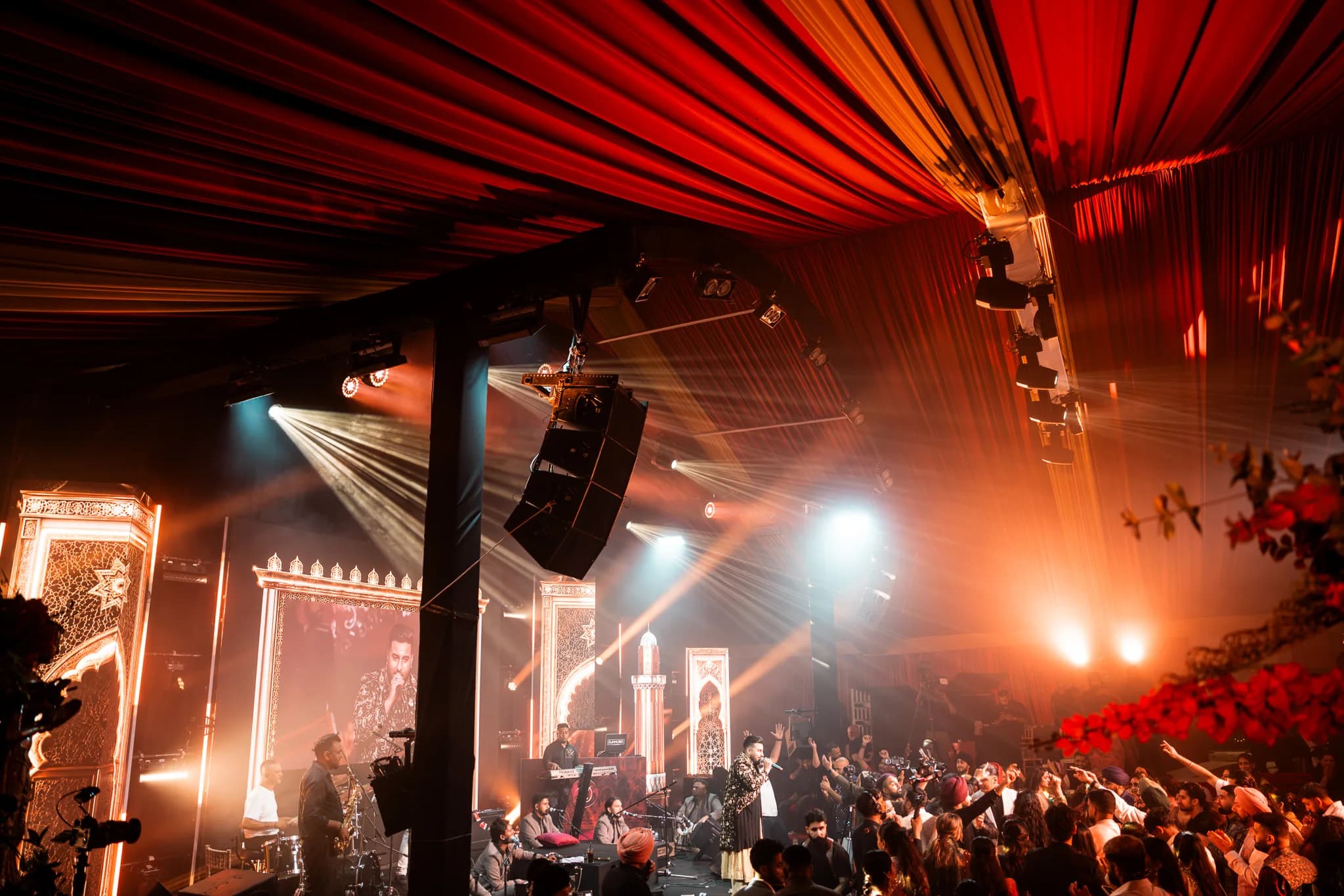 Amber light and haze over the band and the crowd at Eksimran and Dilraj's sangeet, red drapes overhead, Kudos Music
