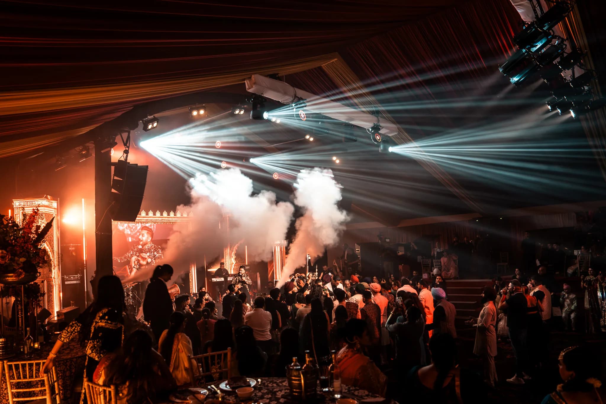 CO2 jets firing over the dancefloor at Eksimran and Dilraj's sangeet, blue beams cutting across the marquee, Kudos Music