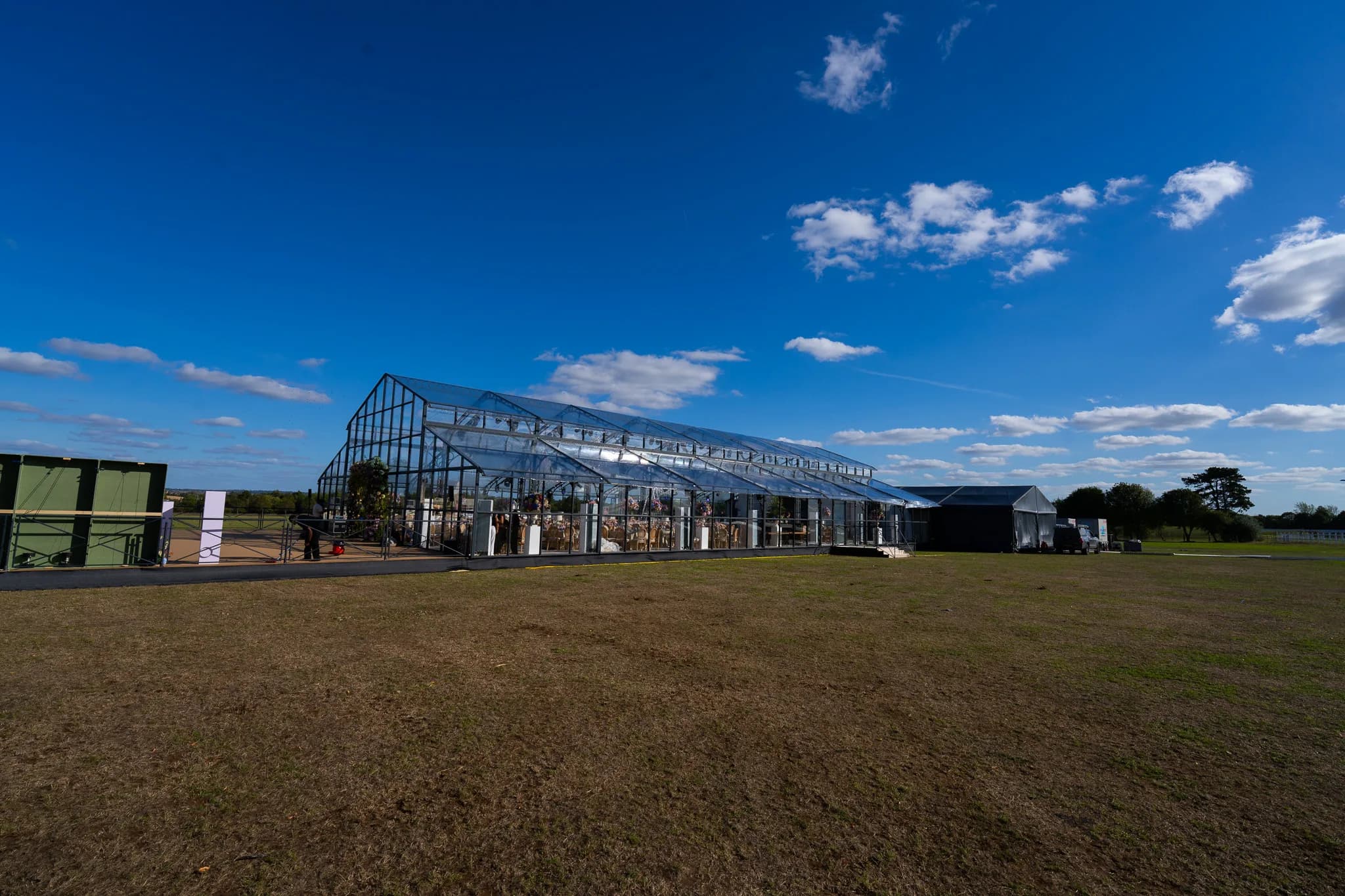 Glass wedding marquee seen across the lawn in afternoon sunshine | Dallas Burston Polo Club Glass wedding marquee seen across the lawn in afternoon sunshine at Dallas Burston Polo Club