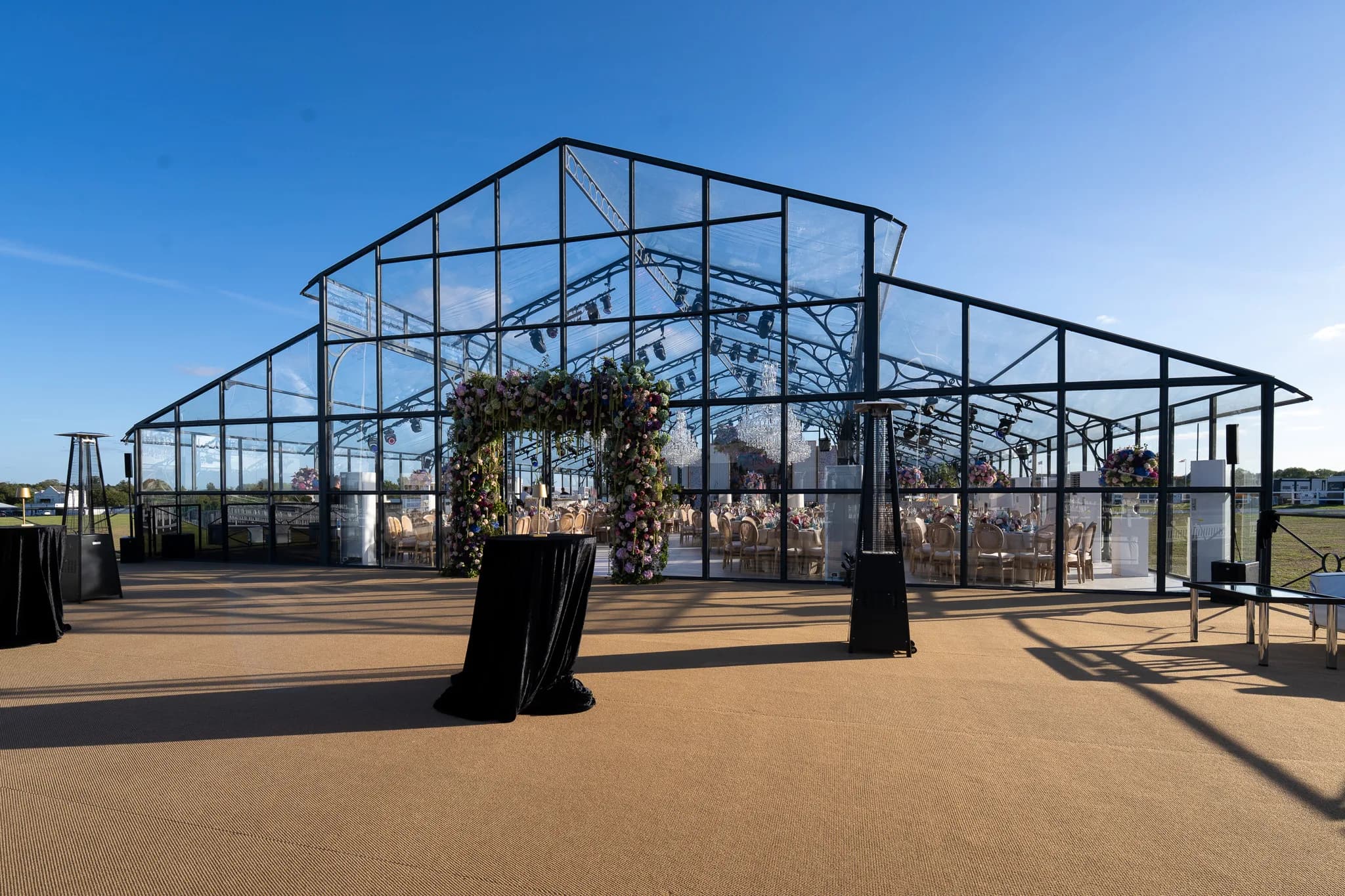 Glass marquee entrance with floral arch and outdoor cocktail tables | Dallas Burston Polo Club Glass marquee entrance with floral arch and outdoor cocktail tables at Dallas Burston Polo Club