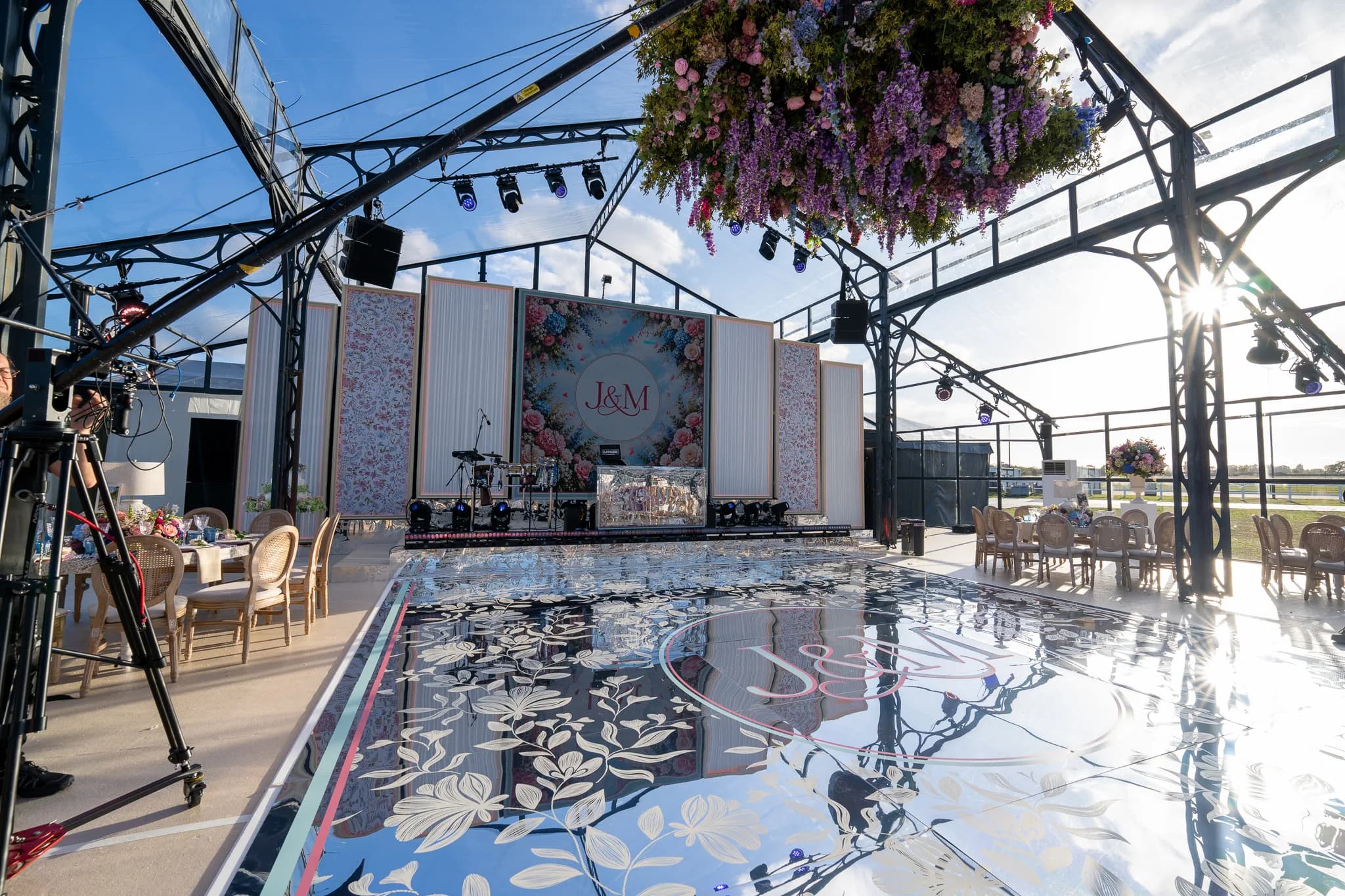The wisteria and hydrangea floral chandelier by Amie Bone hanging over the mirror dancefloor, the sun through the glass and the stage beyond, Jeevan and Megha's wedding at Dallas Burston, Kudos Music