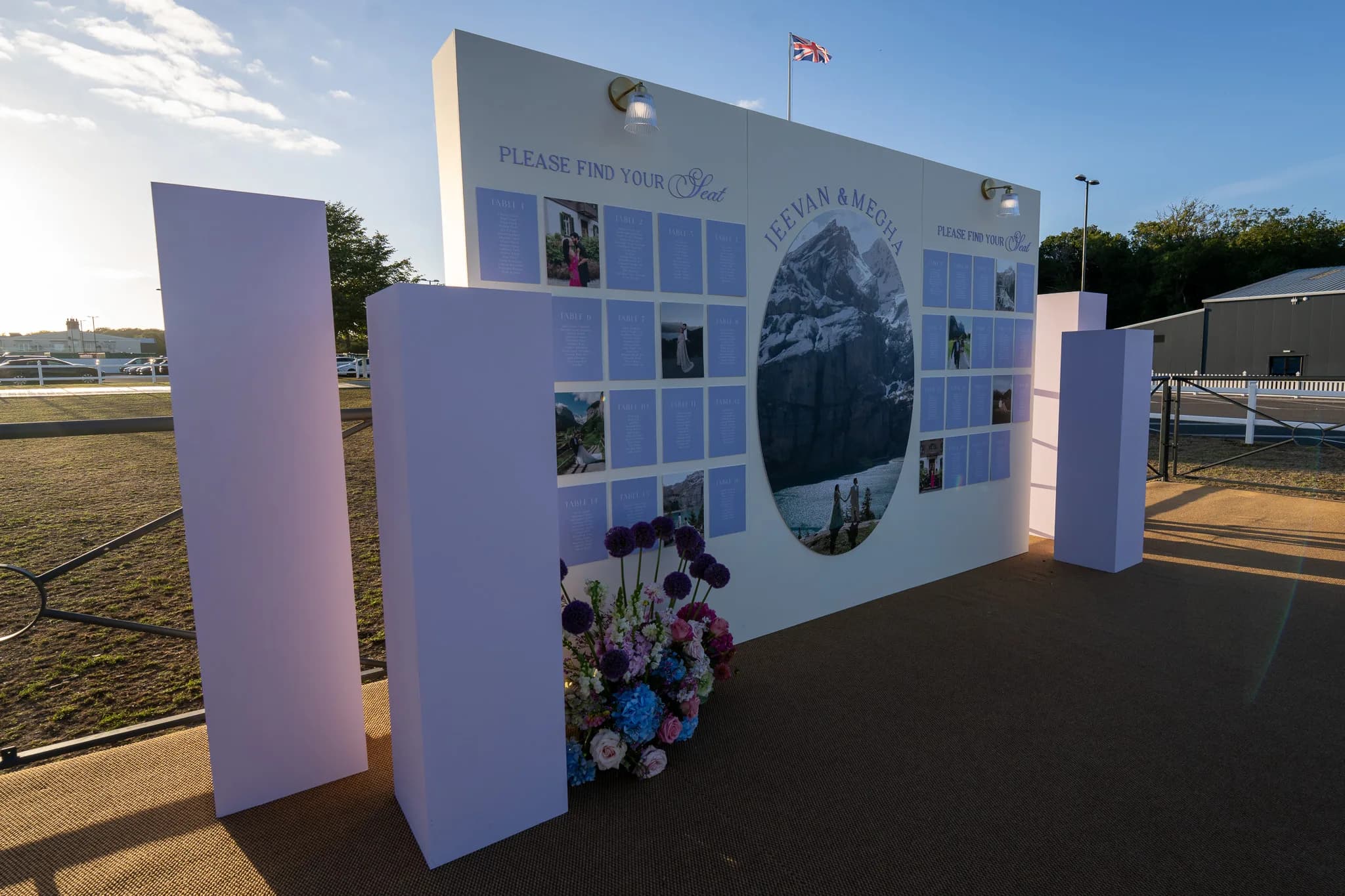 The seating plan wall with the couple photographed in the Alps, lilac plinths and a wildflower arrangement at its foot, Jeevan and Megha's wedding at Dallas Burston Polo Club, Kudos Music