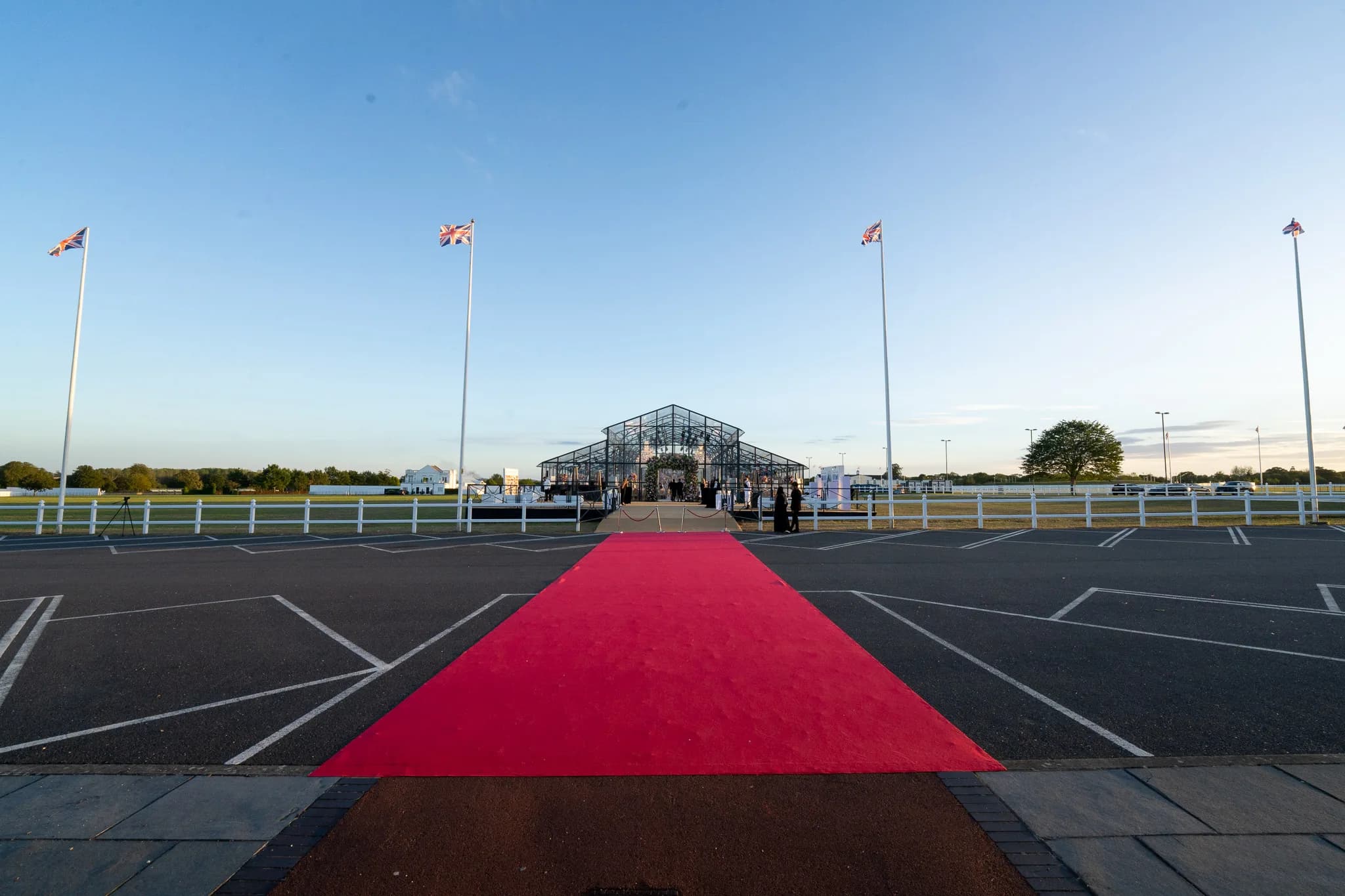 A red carpet running from the car park to the glass marquee under the flagpoles at Dallas Burston Polo Club, the arrival at Jeevan and Megha's wedding, Kudos Music