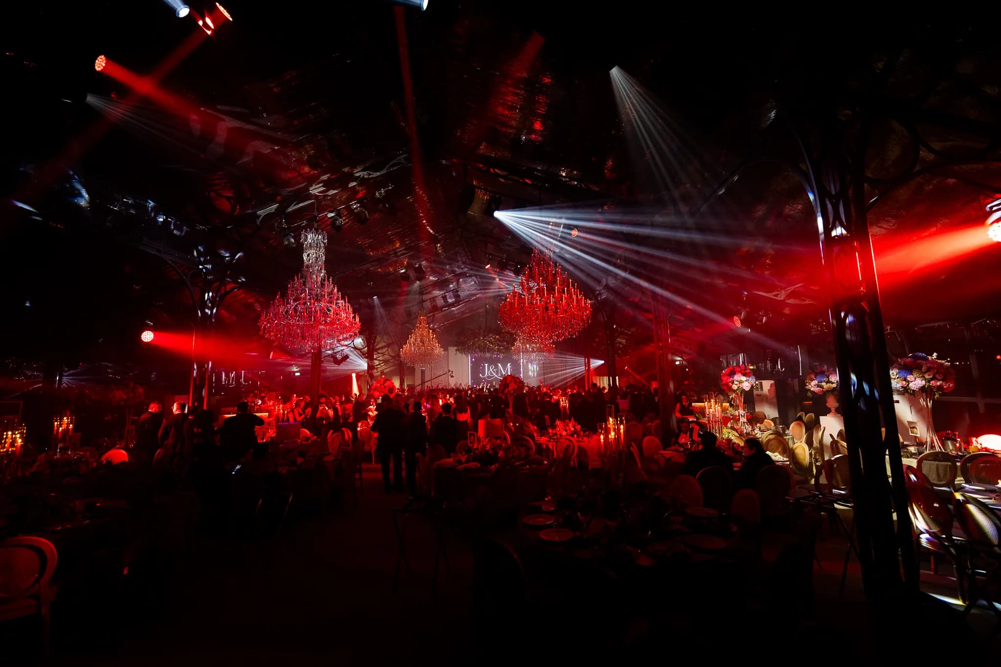 The room in deep red, the chandeliers glowing red and white beams cutting across the glass marquee to the monogram on the screen, Jeevan and Megha's reception at Dallas Burston Polo Club, Kudos Music