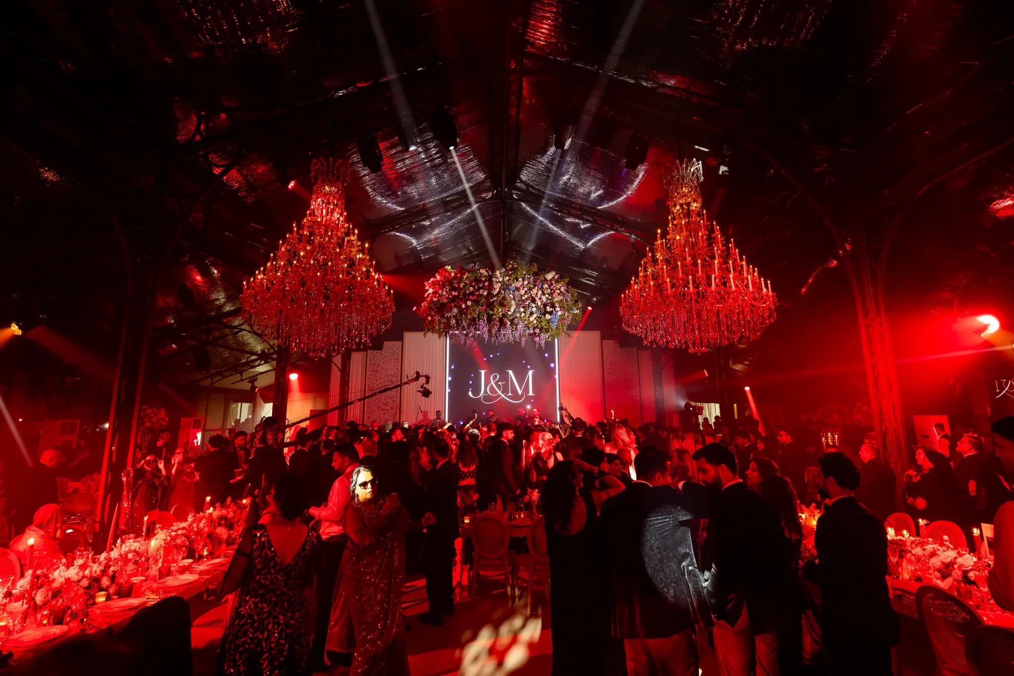Guests on the floor in the red look, the chandeliers lit red, the florals above and the monogram on the screen at the end of the night, Jeevan and Megha's wedding at Dallas Burston, Kudos Music