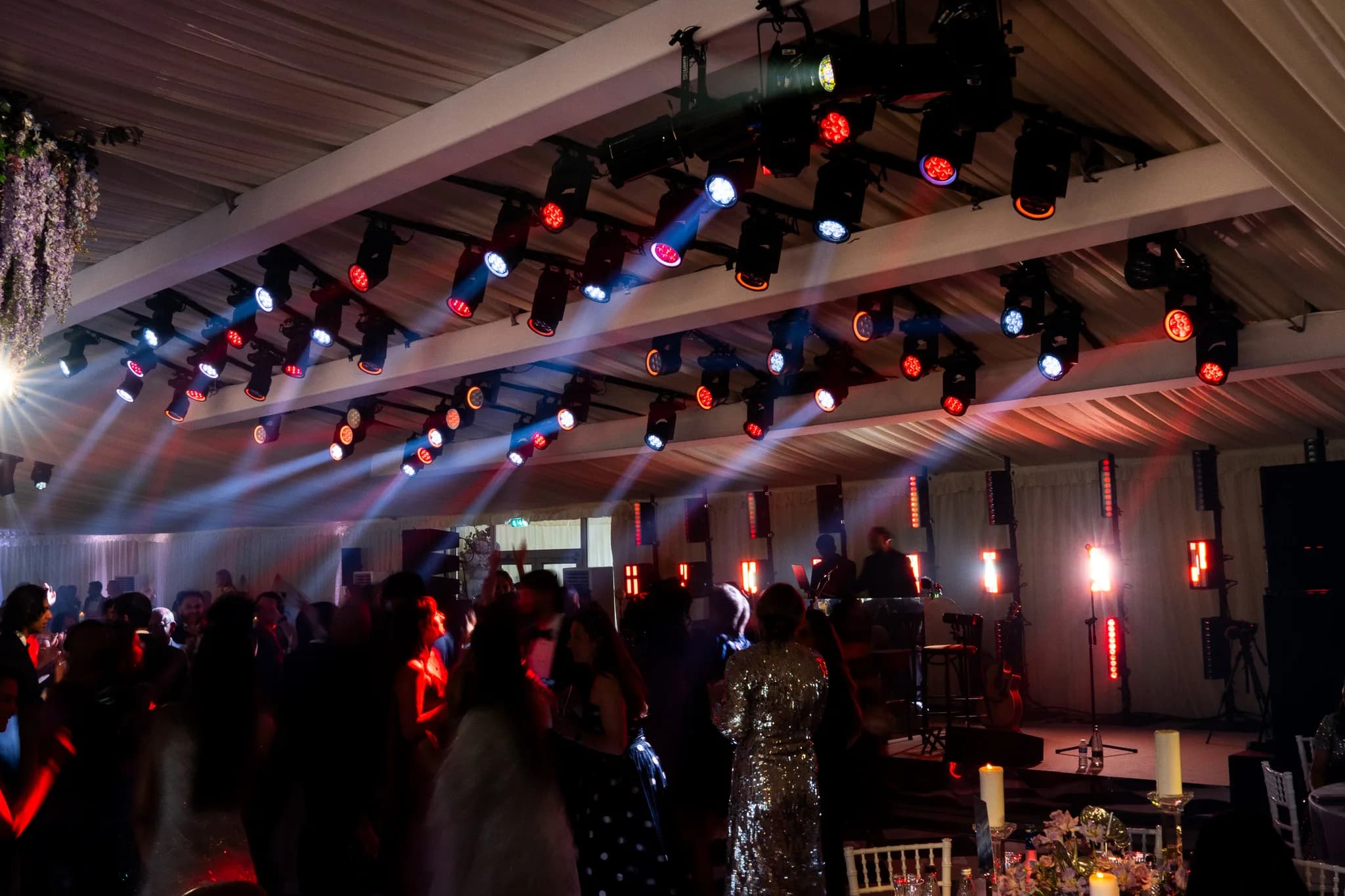Guests dancing under red and blue light with beams cutting across the marquee at Lakhita and Satnaam's Pennyhill Park wedding, Kudos Music