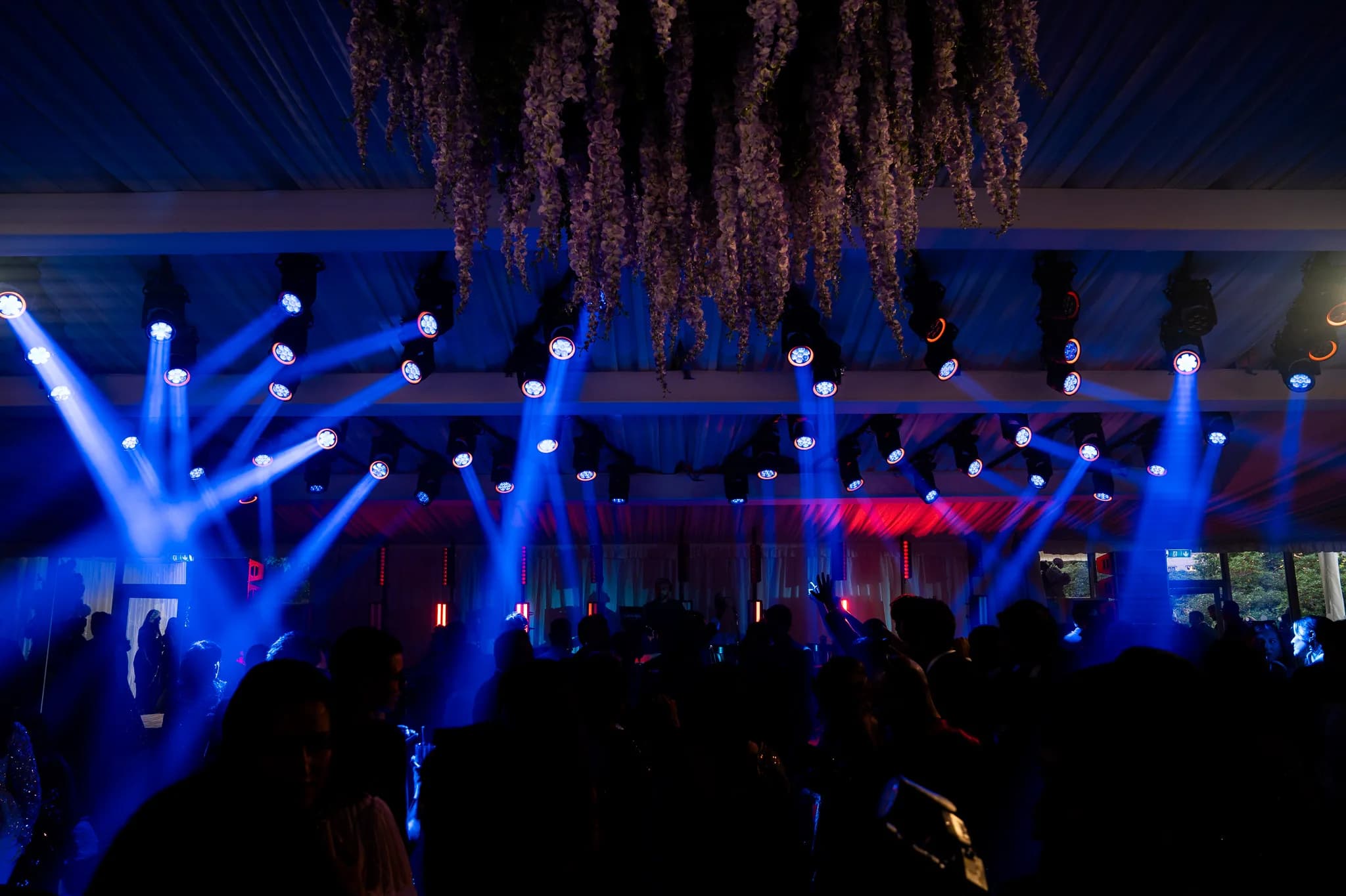 Blue light over a packed dancefloor beneath the hanging florals at Lakhita and Satnaam's marquee wedding, Pennyhill Park, Kudos Music
