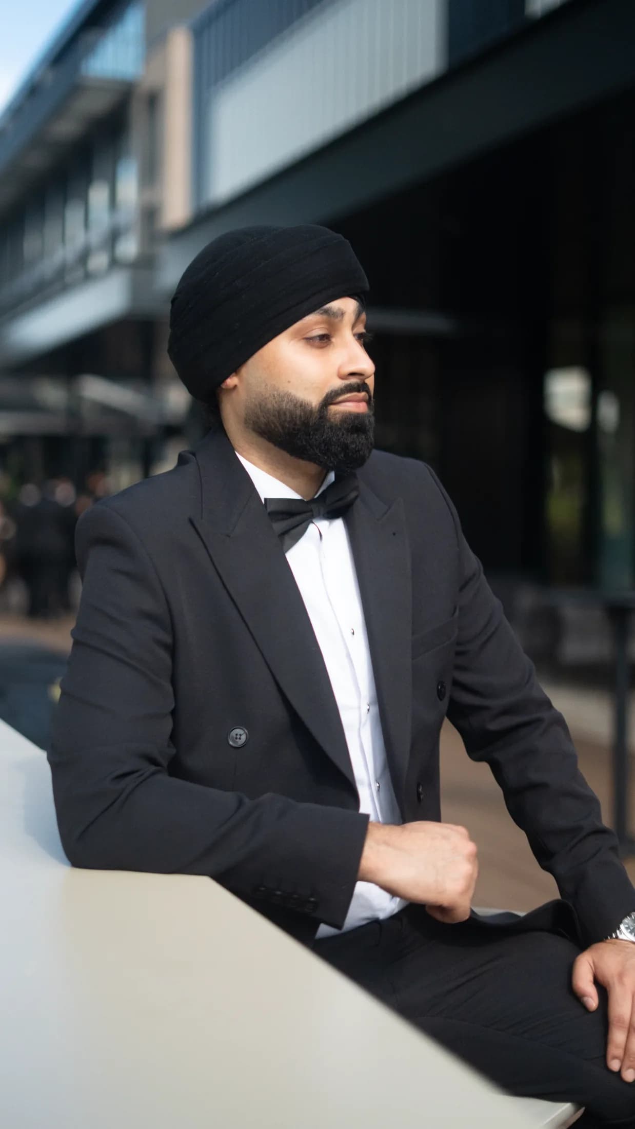 DJ Harj Matharu of Kudos Music in a black tuxedo, leaning on a table and looking to the side