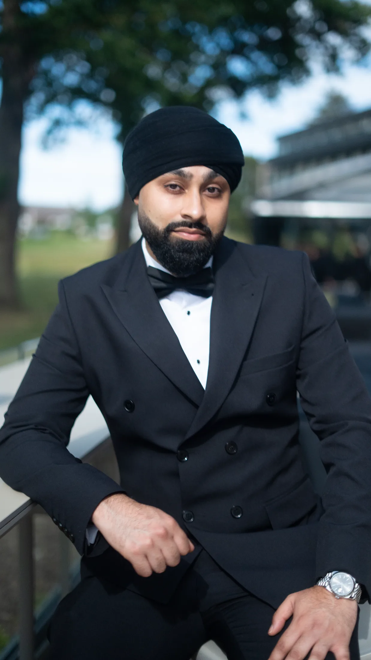DJ Harj Matharu of Kudos Music in black tie, standing outdoors with parkland behind him