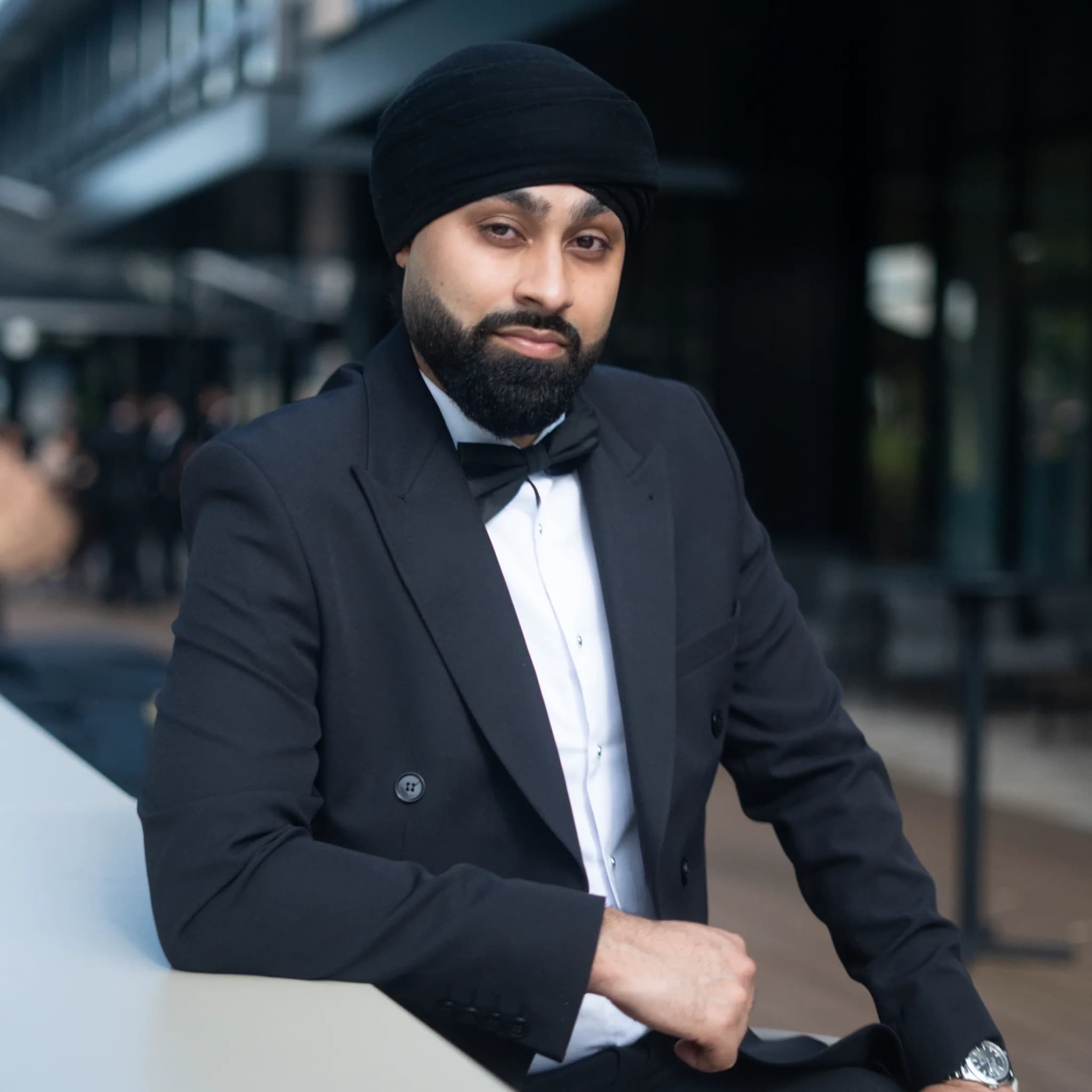 DJ Harj Matharu of Kudos Music in black tie, leaning on a table and looking to camera