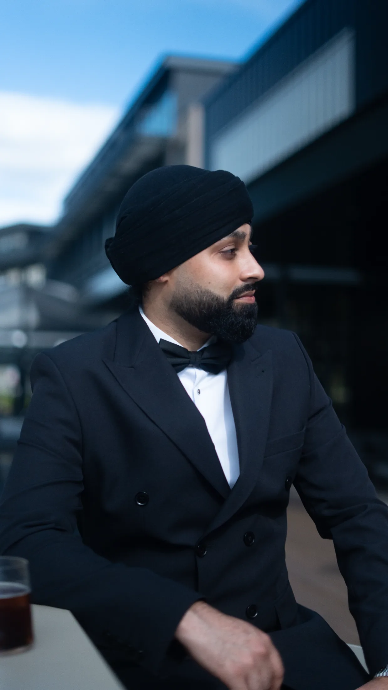 DJ Harj Matharu of Kudos Music in a black tuxedo, turned away in profile outdoors
