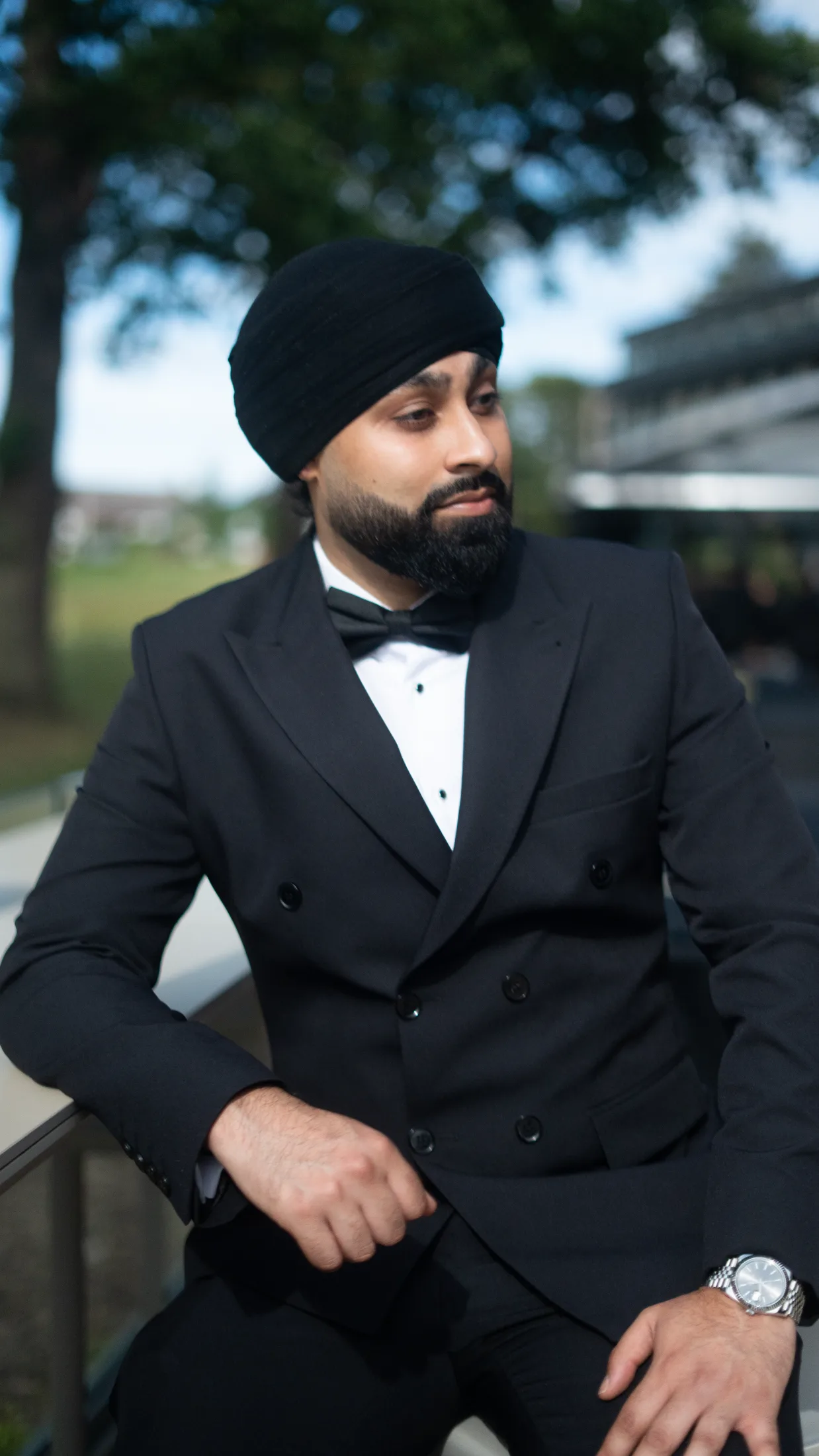 DJ Harj Matharu of Kudos Music in a black tuxedo and turban, looking down with trees behind him