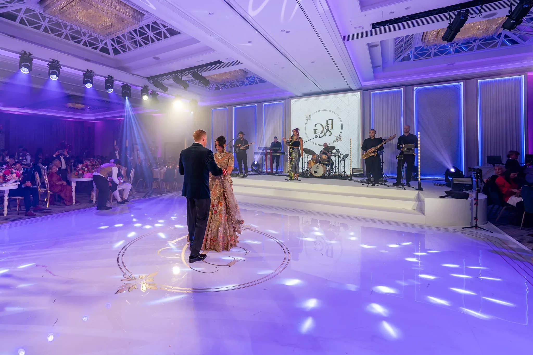 Pooja and Gary sharing their first dance on a monogrammed white floor under violet light at Royal Lancaster London.