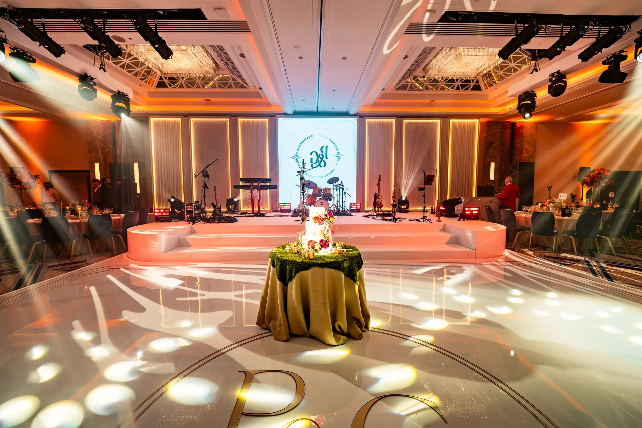 Their names on the floor | Royal Lancaster London | Kudos Music Pooja and Gary’s monogram on the white dancefloor, with the illuminated wedding stage behind.