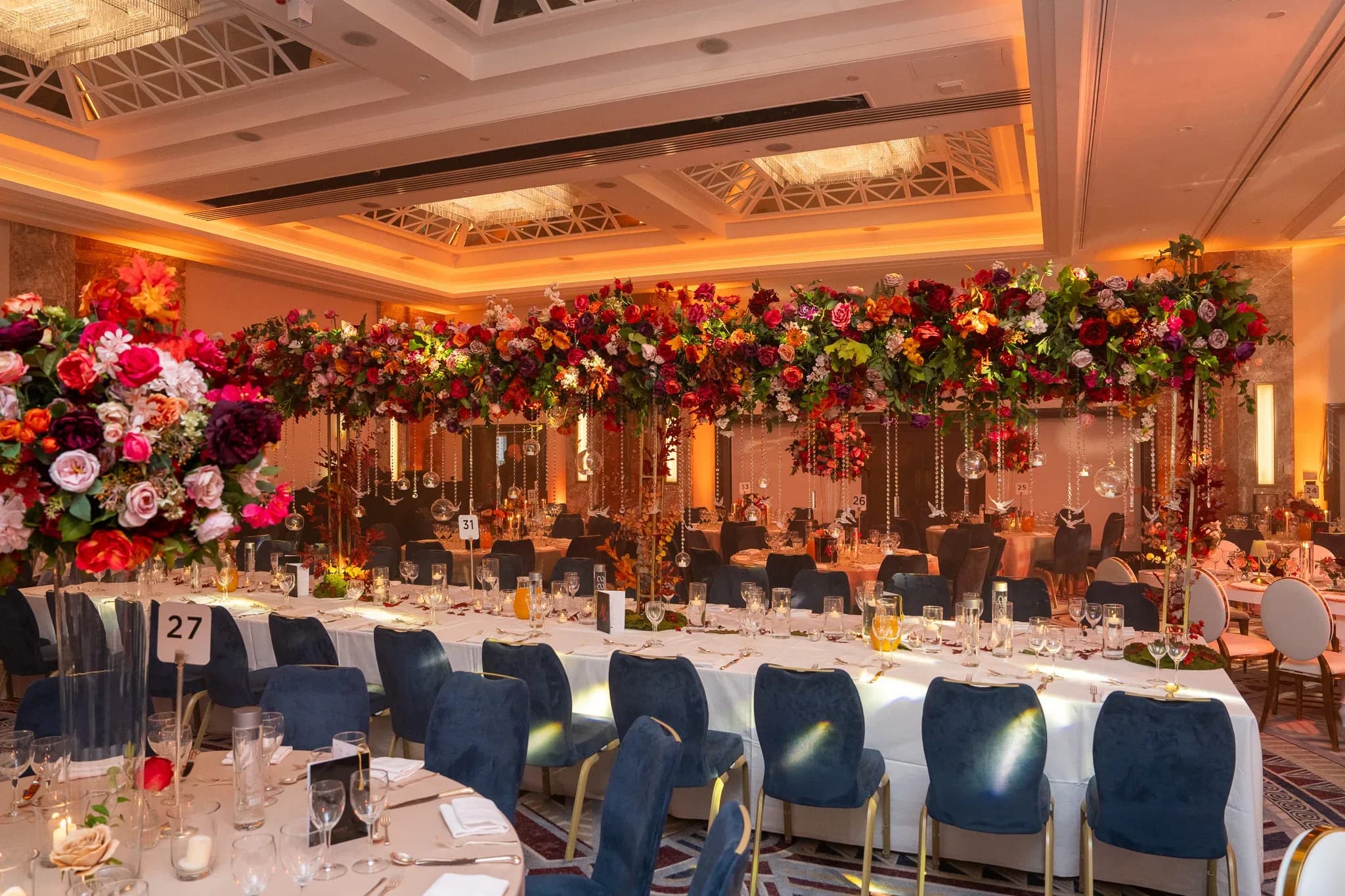 Around the table | Royal Lancaster London | Kudos Music Banquet tables with blue chairs and red floral canopies at Pooja and Gary’s Royal Lancaster London wedding.