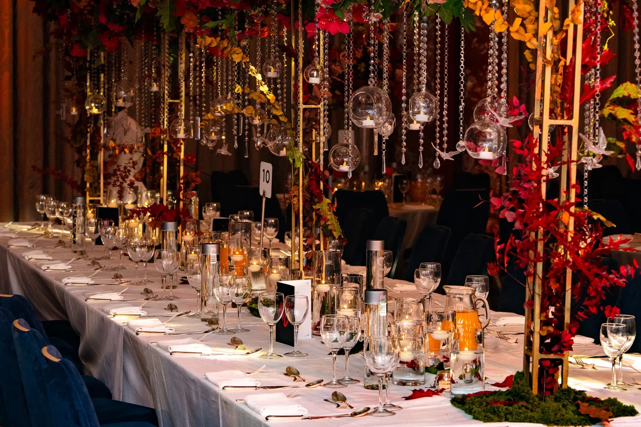 Dinner among the flowers | Royal Lancaster London | Kudos Music Hanging candles and red flowers above a long wedding table at Royal Lancaster London.