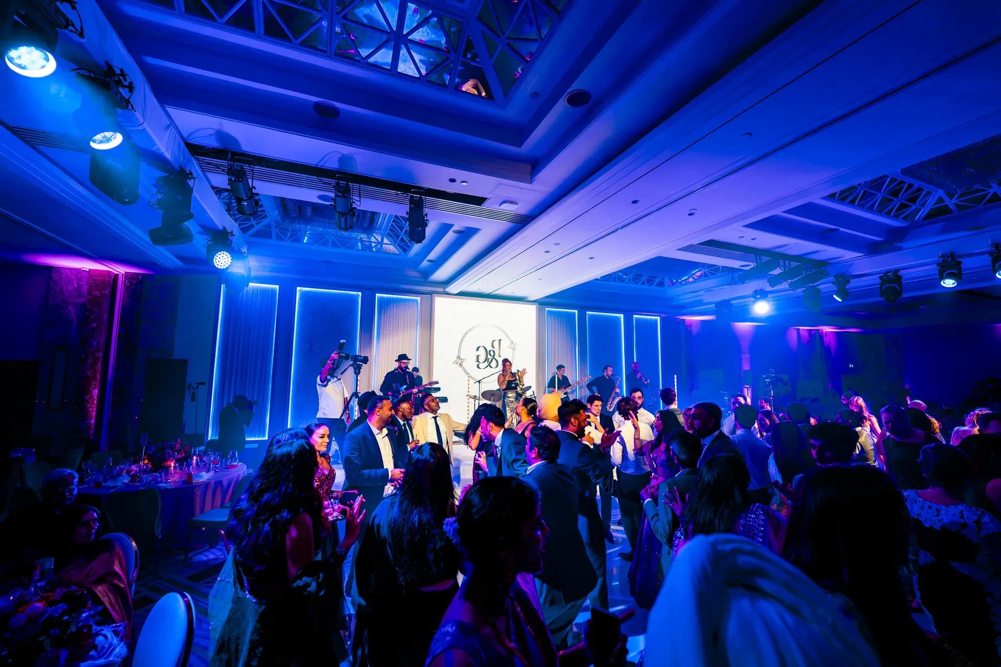 A busy wedding dancefloor under blue light at Royal Lancaster London, during Pooja and Gary’s celebration.