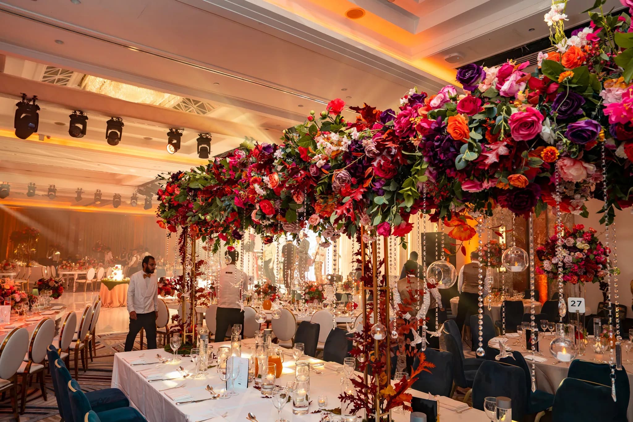 Flowers above the tables | Royal Lancaster London | Kudos Music A red floral canopy above the dining space, with warm lighting across the Royal Lancaster London ballroom.