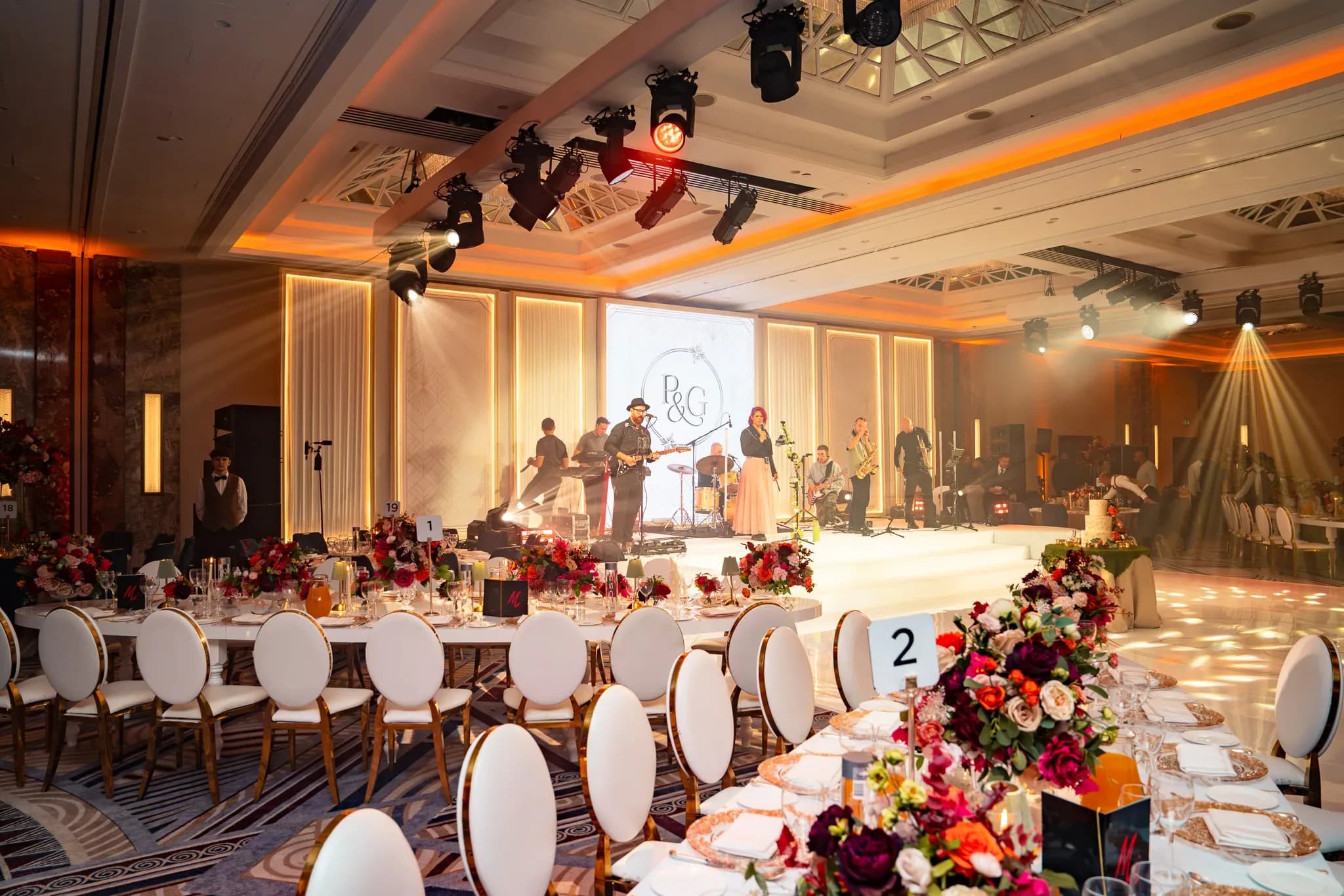 Music in the room | Royal Lancaster London | Kudos Music Musicians performing on the white stage at Pooja and Gary’s wedding, with their monogram on the screen behind.