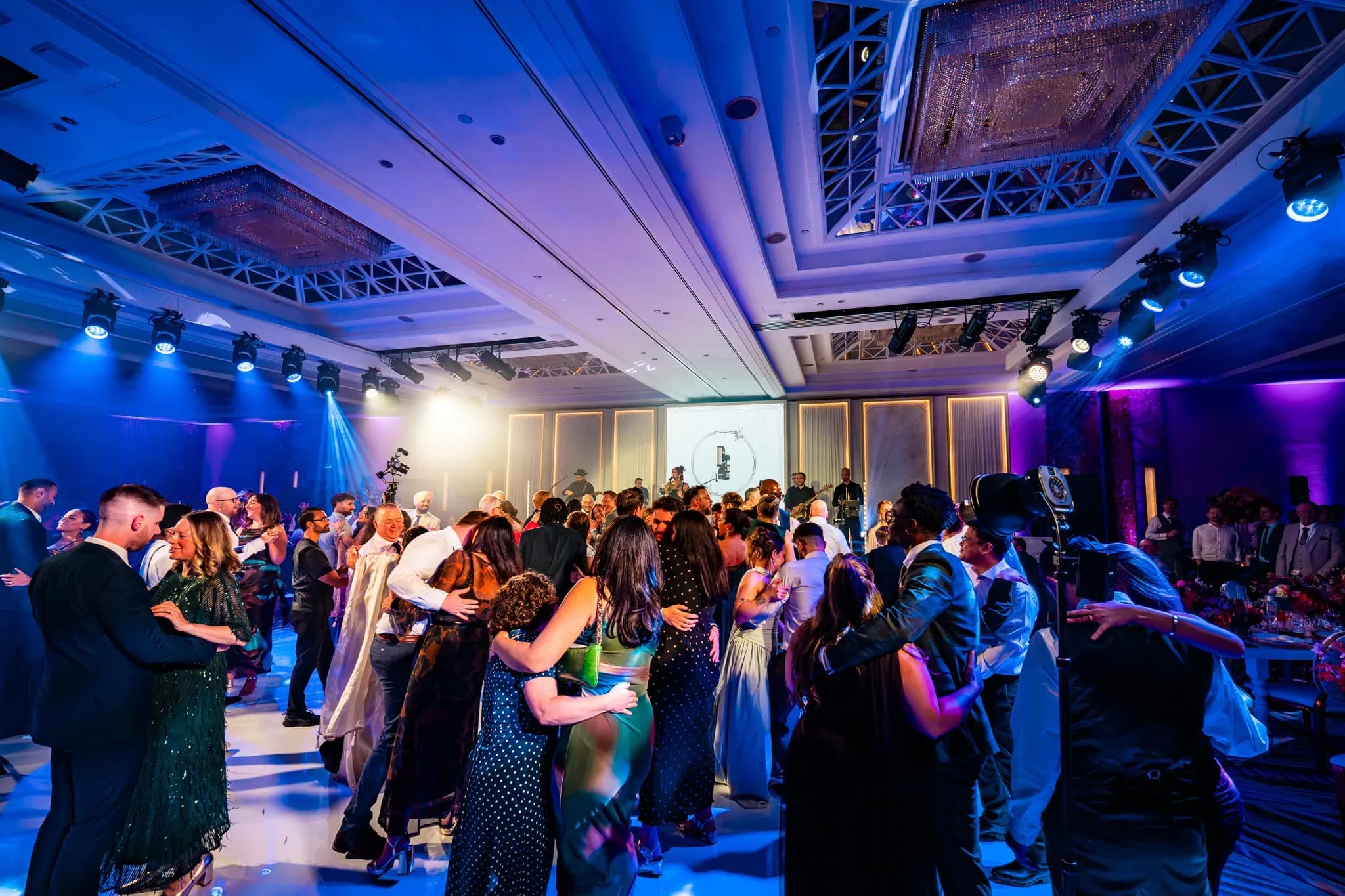 Friends and family dancing together under blue and violet lights at Pooja and Gary’s Royal Lancaster London wedding.