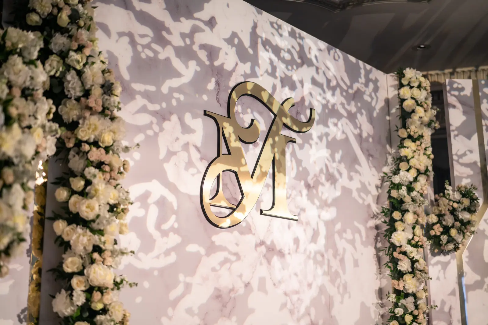 Gold monogram on a white marble-effect wedding backdrop with flowers at The Dorchester