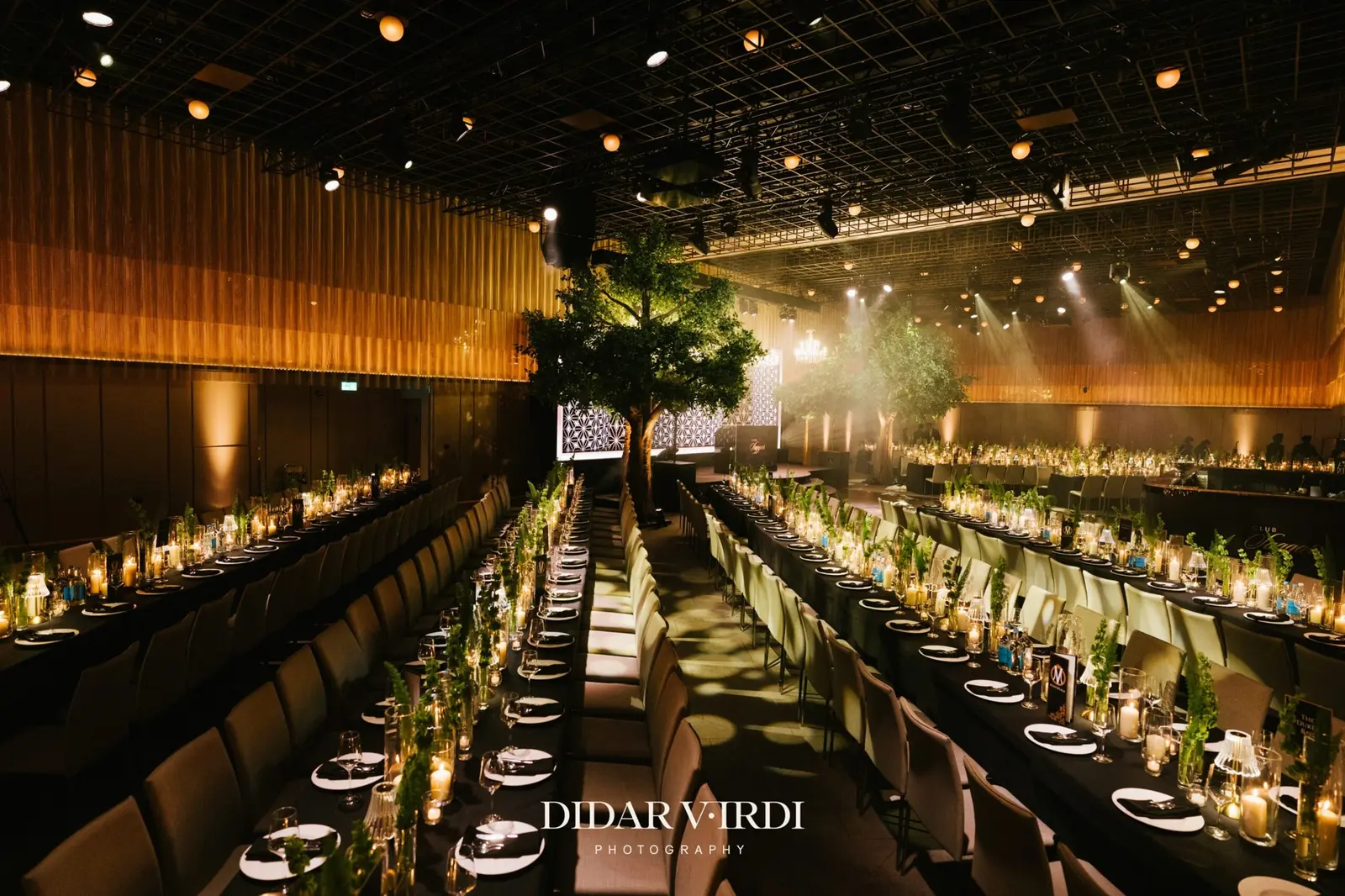 Long candlelit wedding tables leading to a stage framed by trees and LED panels at The Londoner