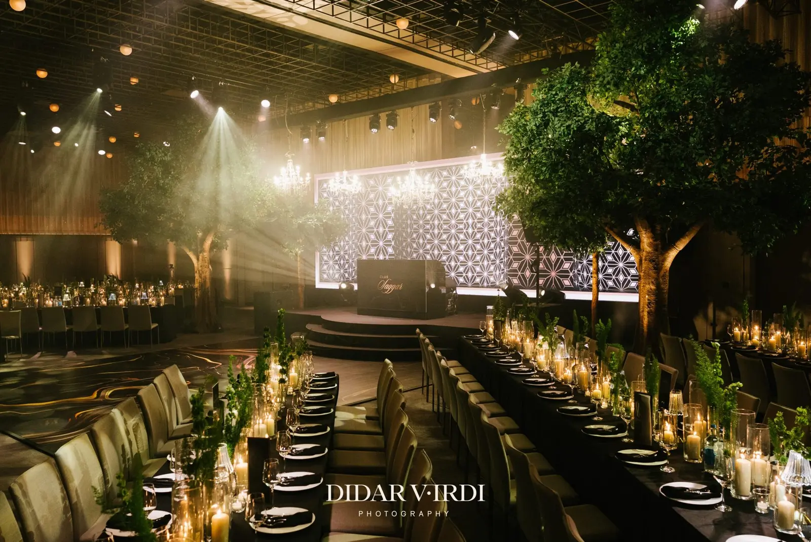 Warm stage beams above long wedding tables and tree-lined scenery at The Londoner