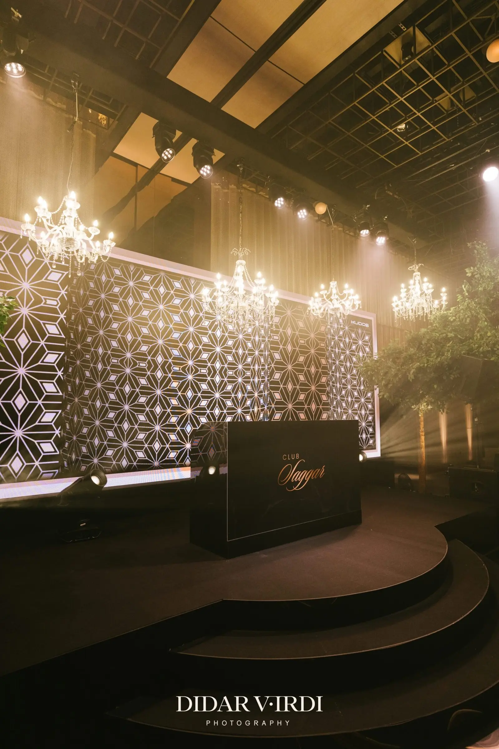 Curved stage steps beneath chandeliers and a patterned LED screen | The Londoner Curved stage steps beneath chandeliers and a patterned LED screen at The Londoner