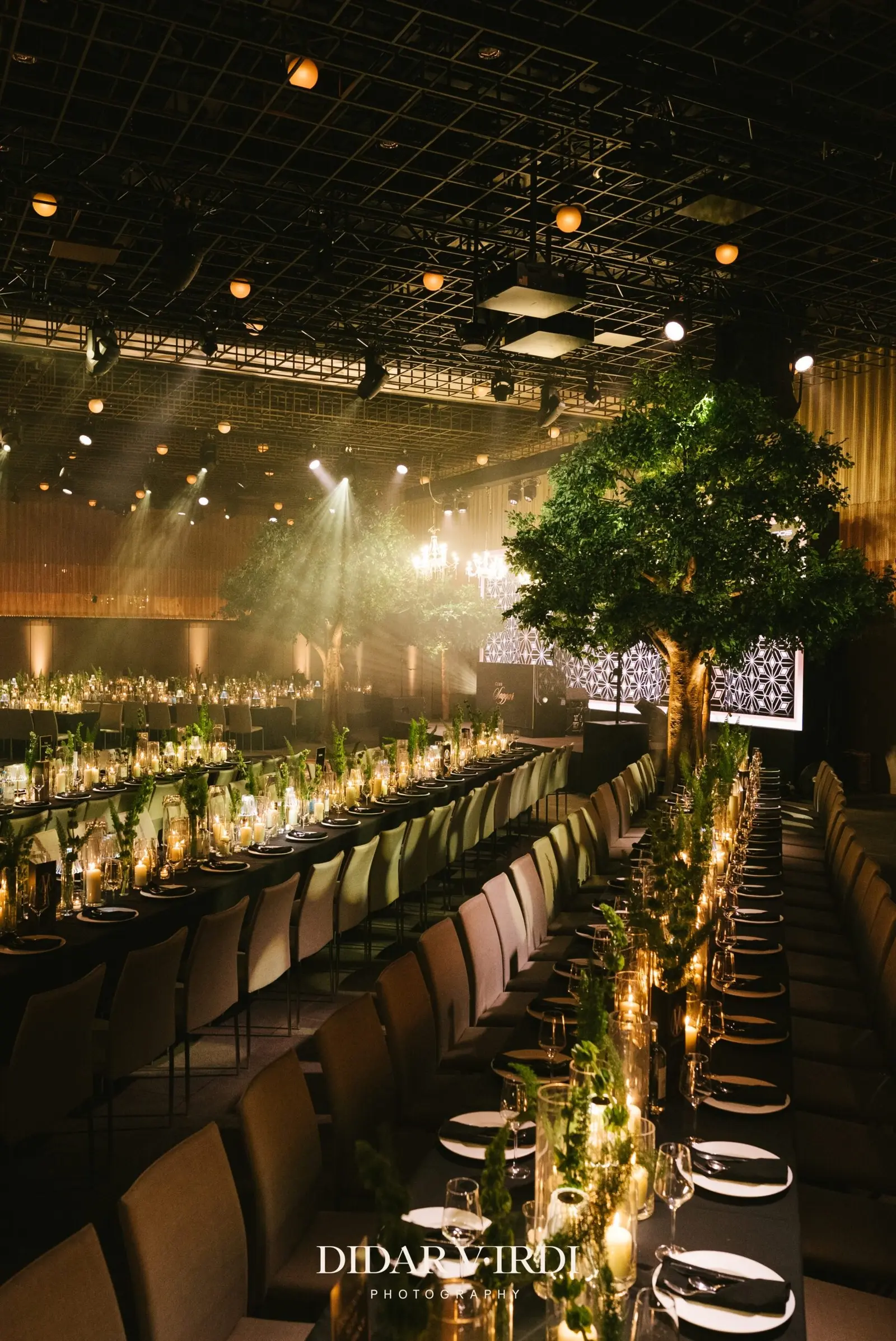 Long rows of candlelit reception tables viewed towards the stage | The Londoner Long rows of candlelit reception tables viewed towards the stage at The Londoner